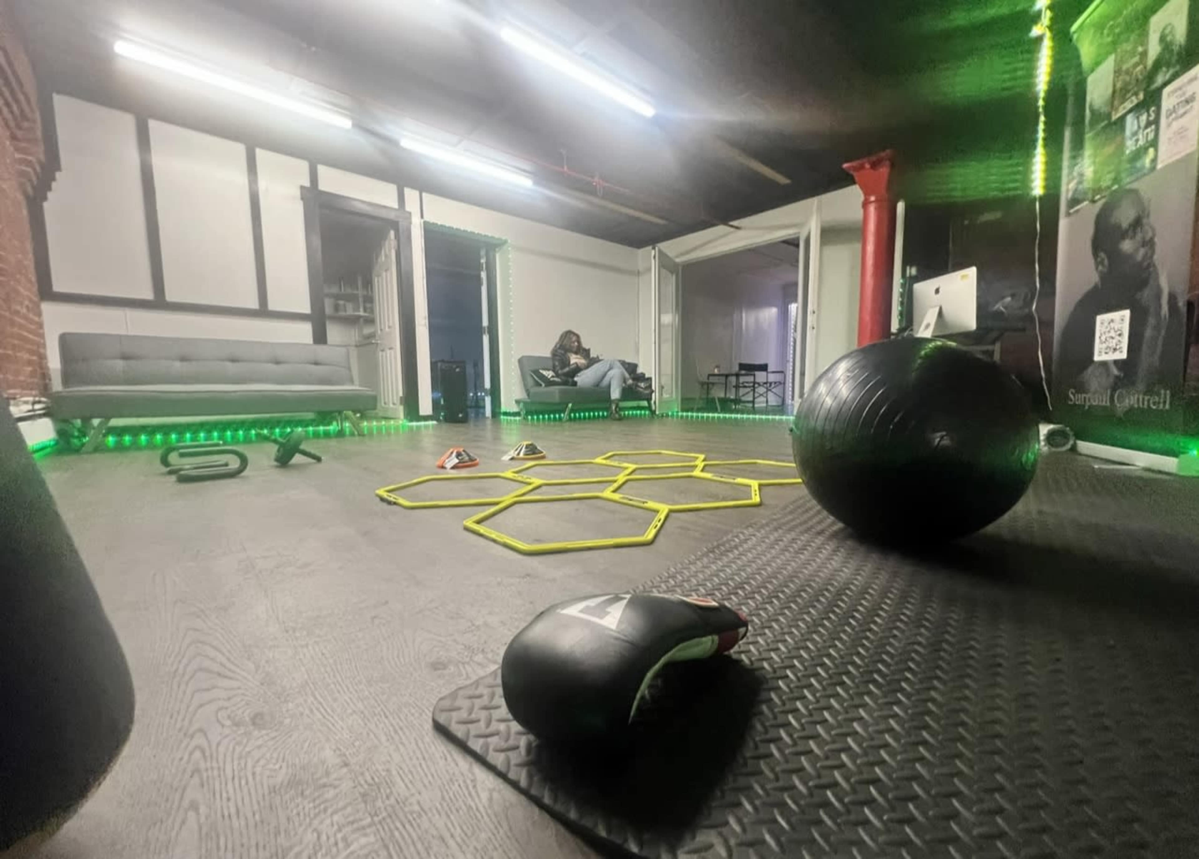 A fitness studio features workout equipment, including a stability ball and agility ladder, set against a backdrop of green LED lights.