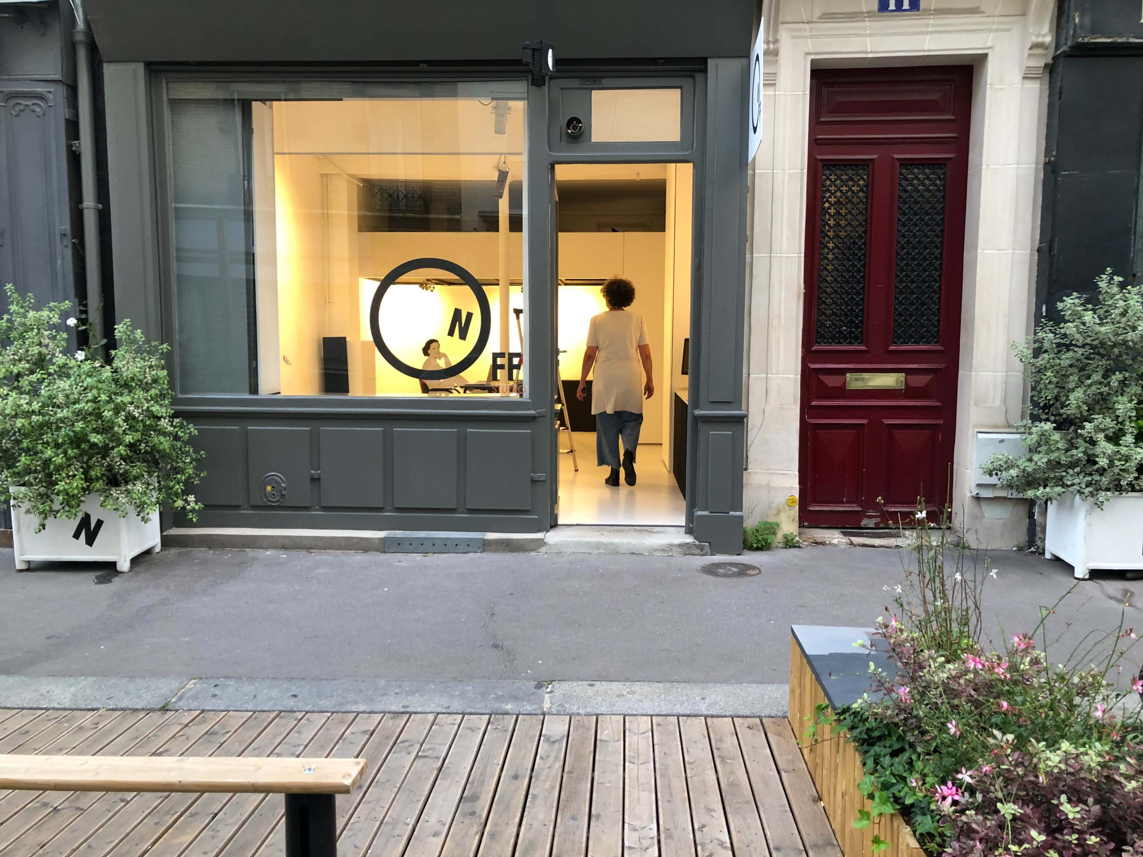 A person walks into a modern office space with large windows and a visible logo, located on a city street.
