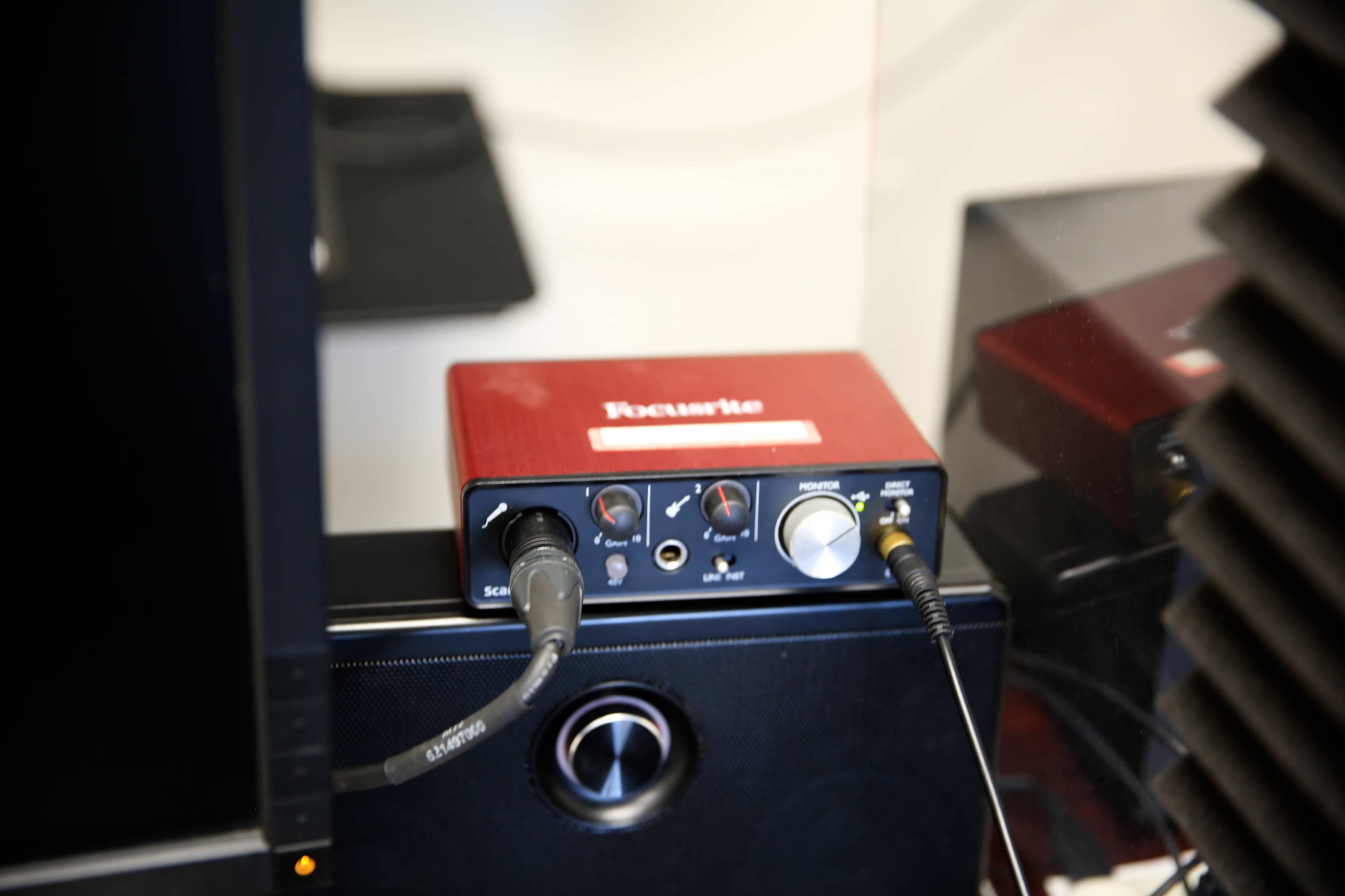 A red audio interface is positioned on top of a black speaker, with cables connected to it.
