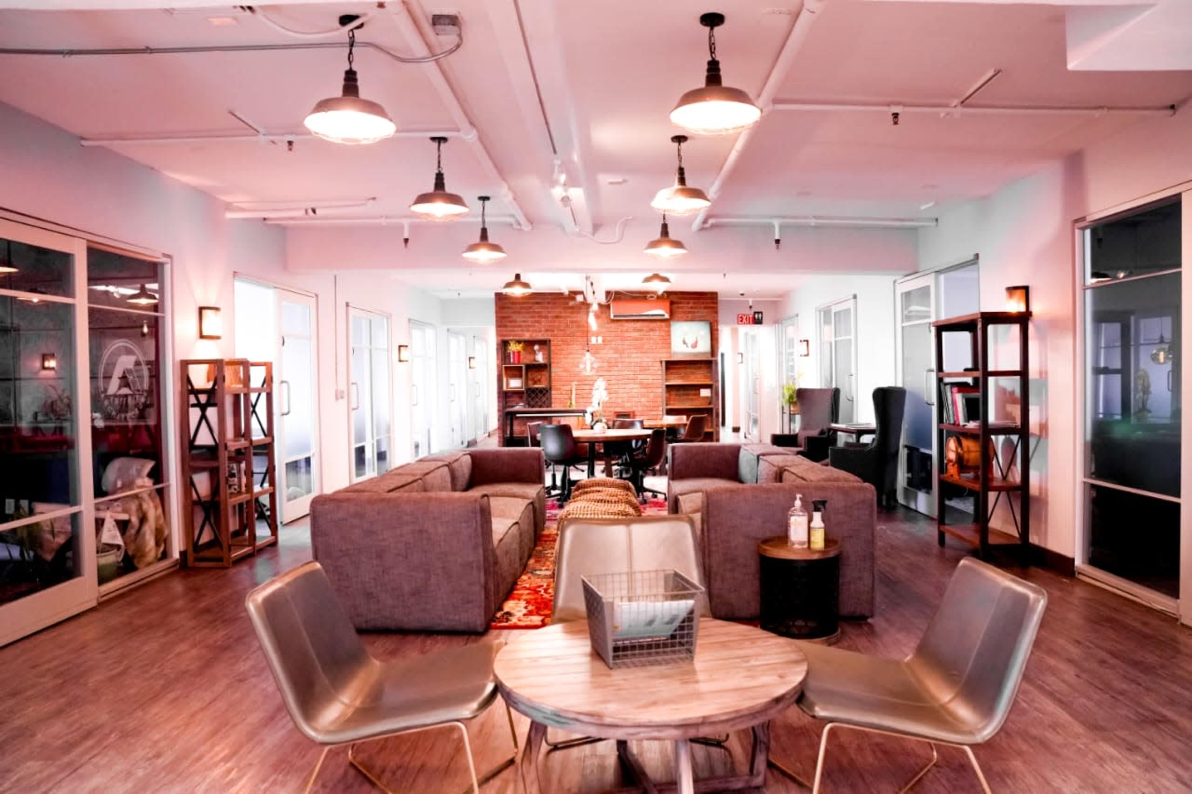A modern common area features gray sofas, a wooden table, and bookshelves in an open-plan office space.