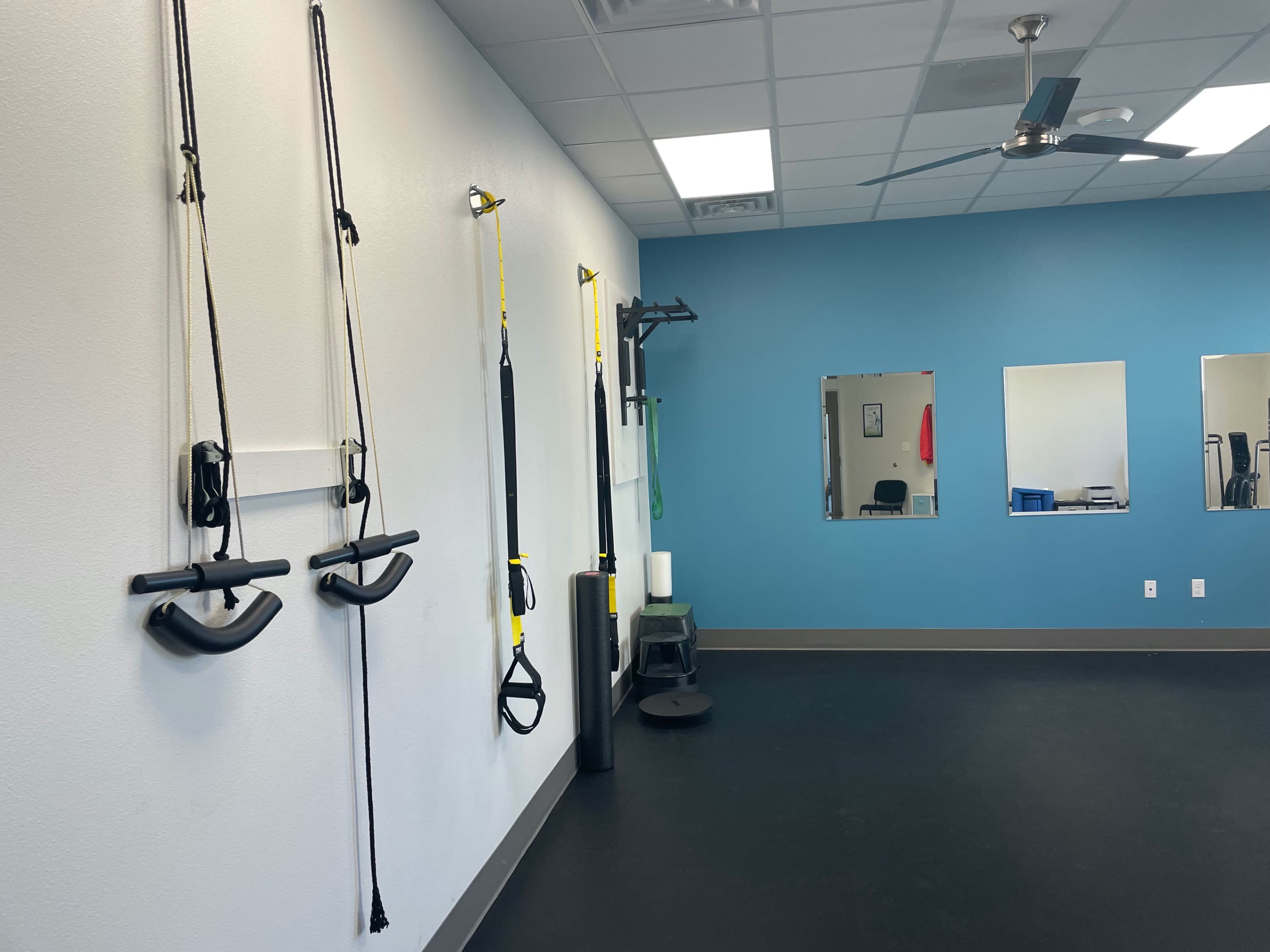 A fitness room with exercise equipment mounted on the walls and mirrors reflecting the interior features.