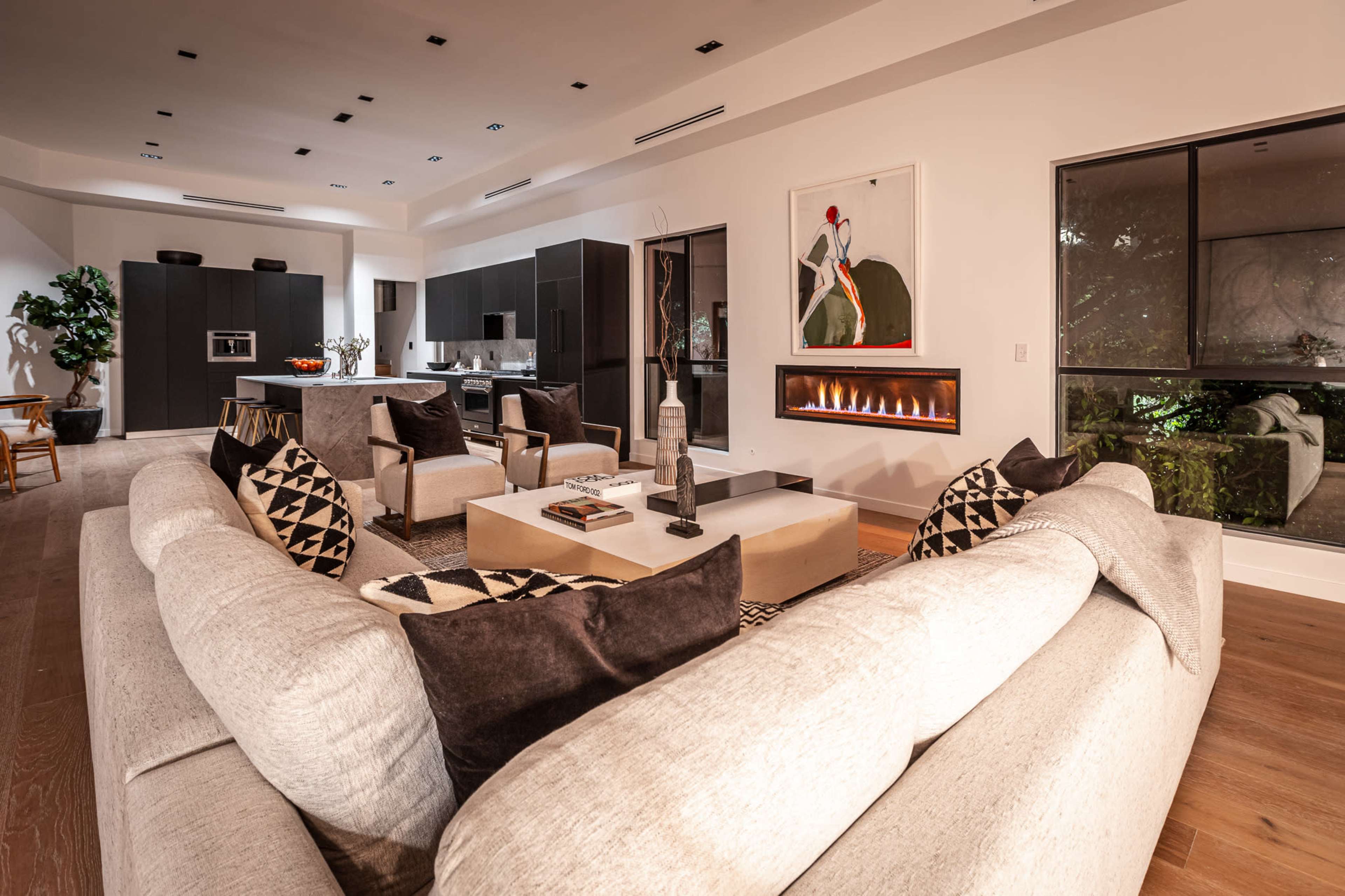 A modern living room with a large sectional sofa facing a fireplace and an open kitchen in the background.