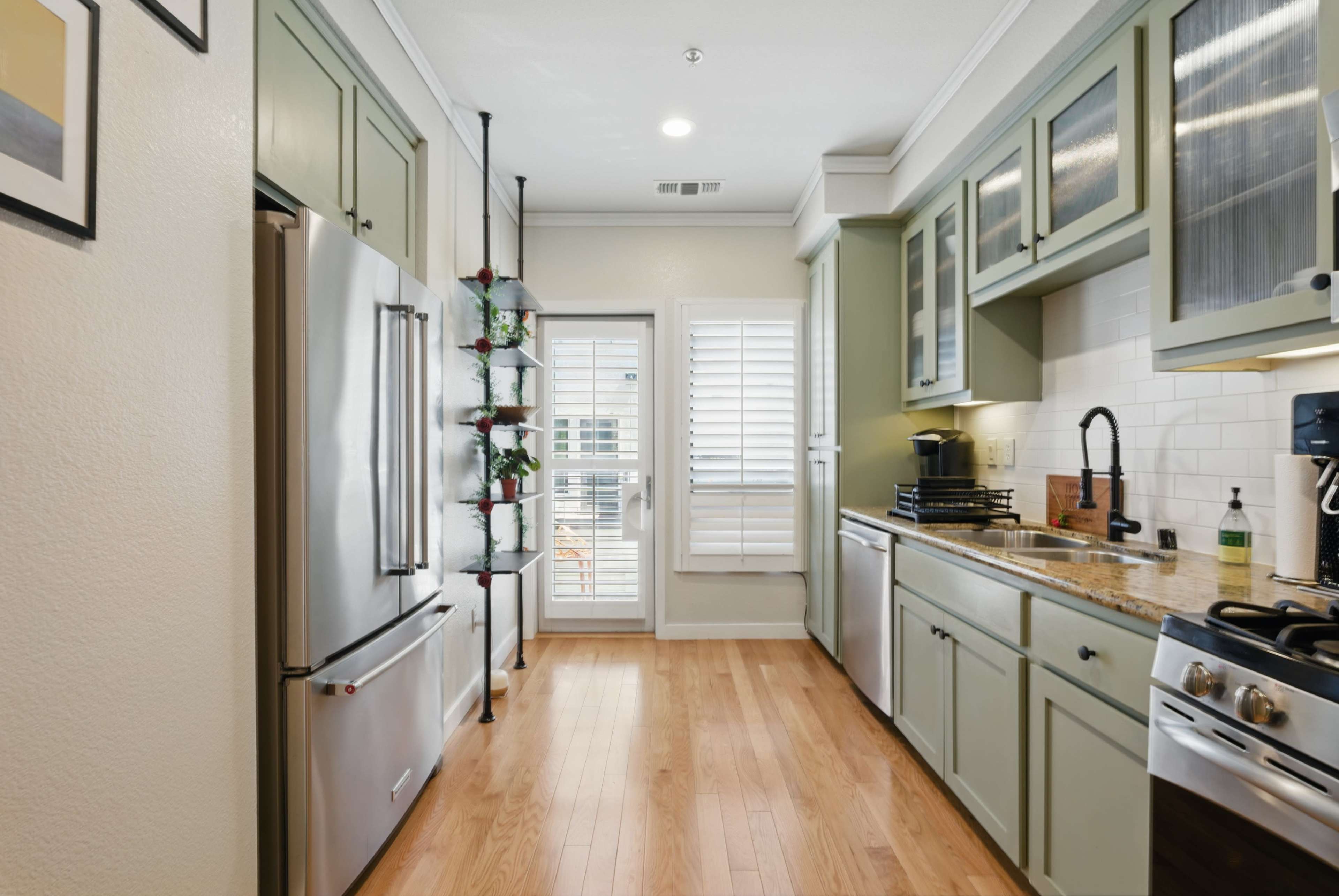 The image shows a modern kitchen featuring green cabinetry, stainless steel appliances, and a large window that provides natural light.