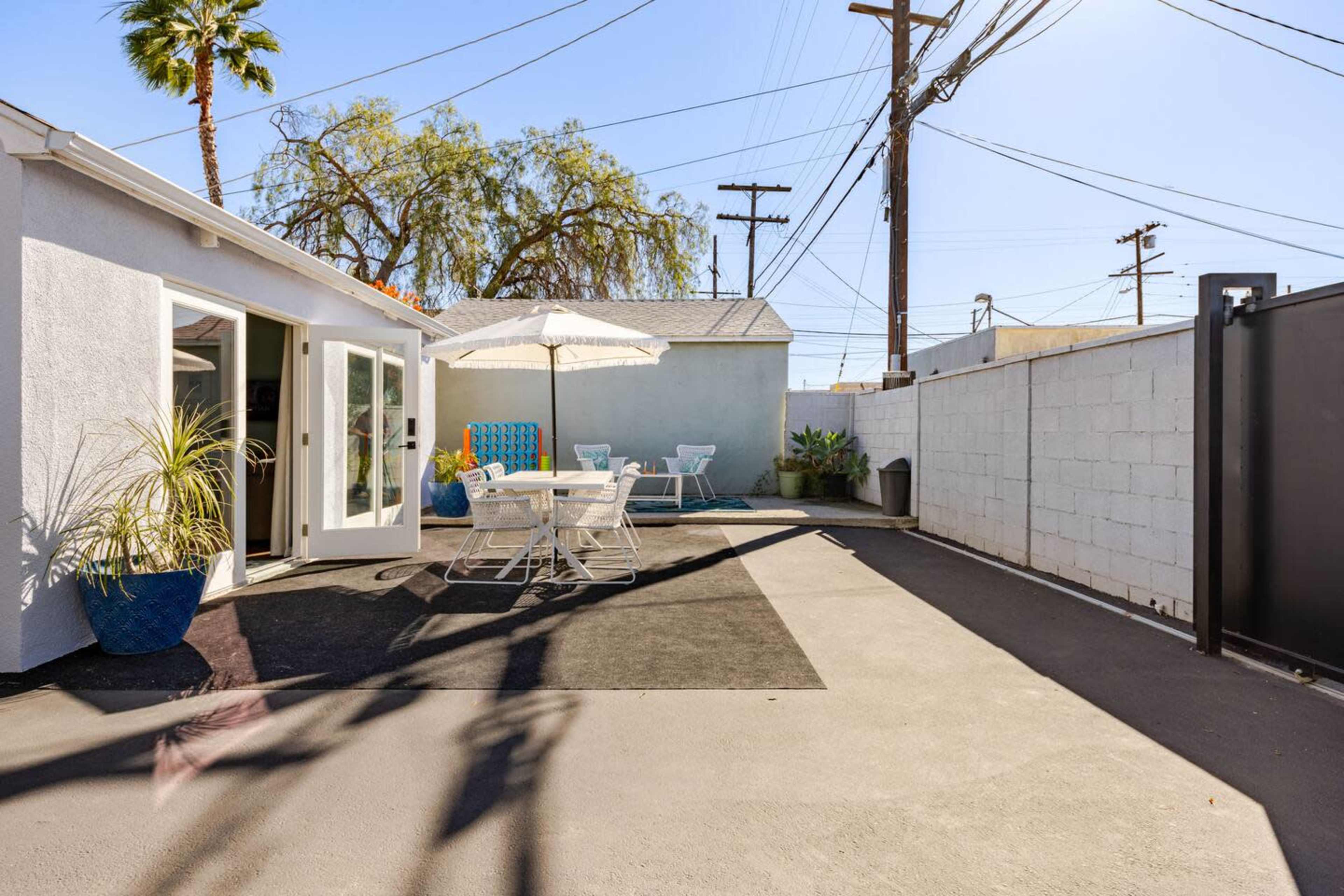 The image shows a landscaped outdoor space with a patio featuring a table and chairs, an umbrella, and a small pool area surrounded by plants and a wall.