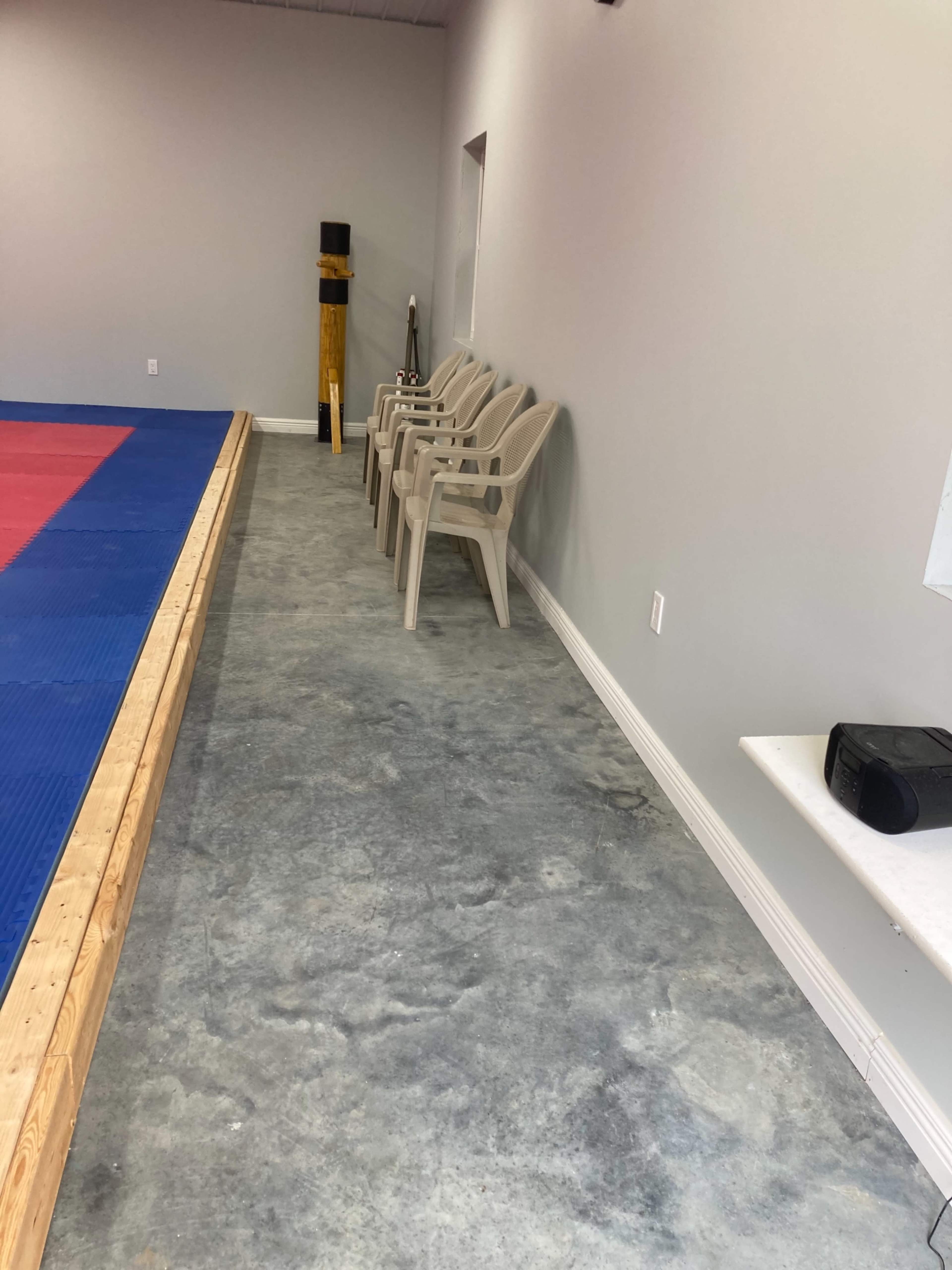 A row of plastic chairs along a concrete floor beside a mat-covered area in a training space.