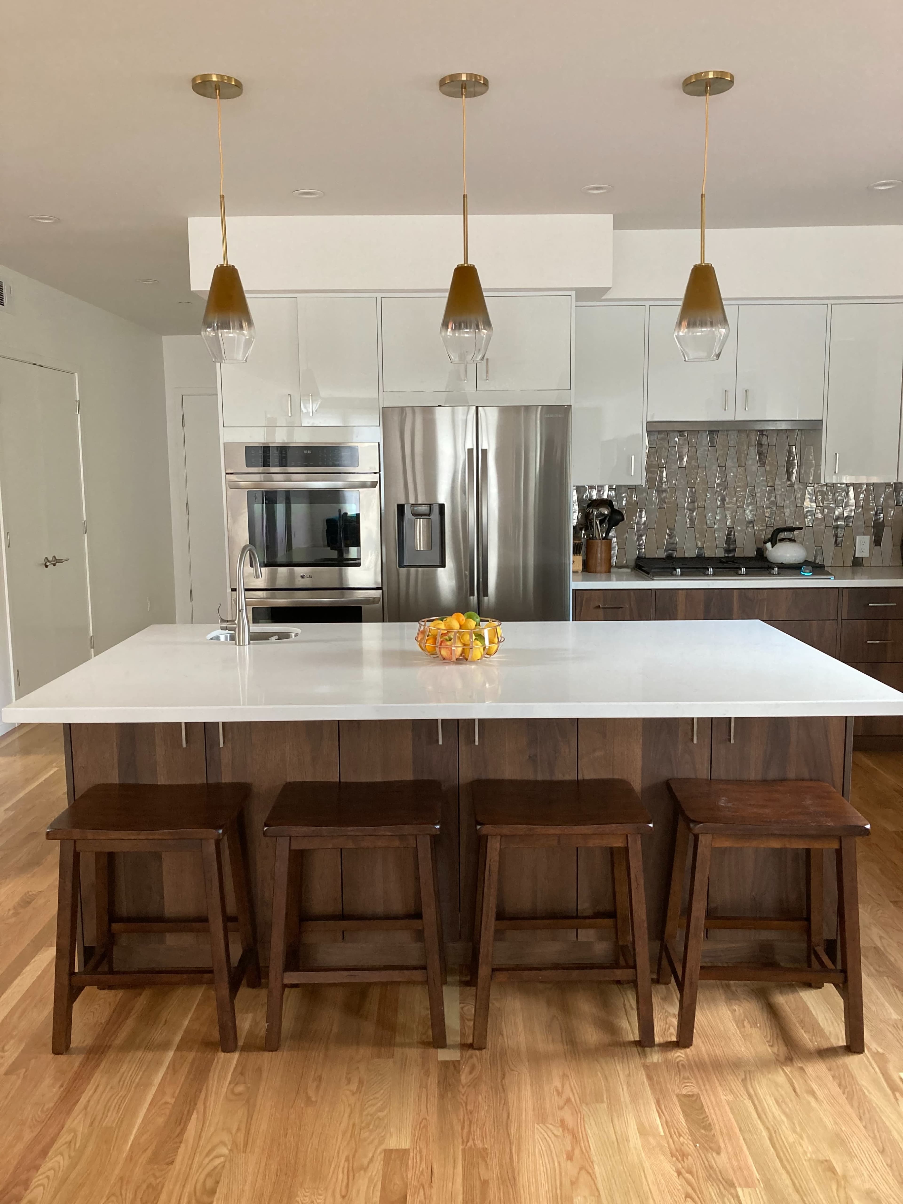 A modern kitchen featuring a large island with a white countertop, four wooden stools, and pendant lighting above.