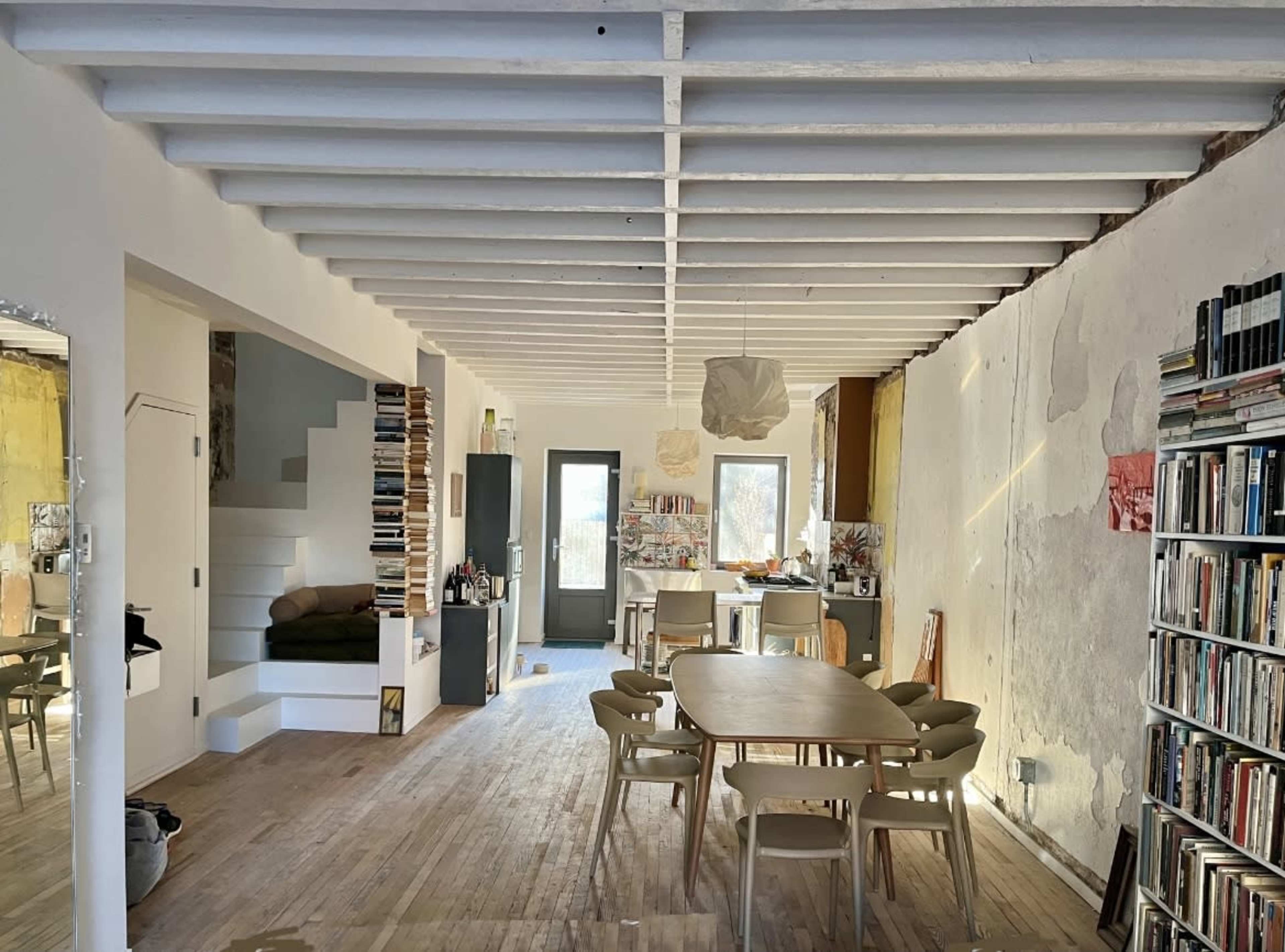 The image shows a modern interior space with large windows, wooden flooring, and minimalist decor featuring furniture and wall art.