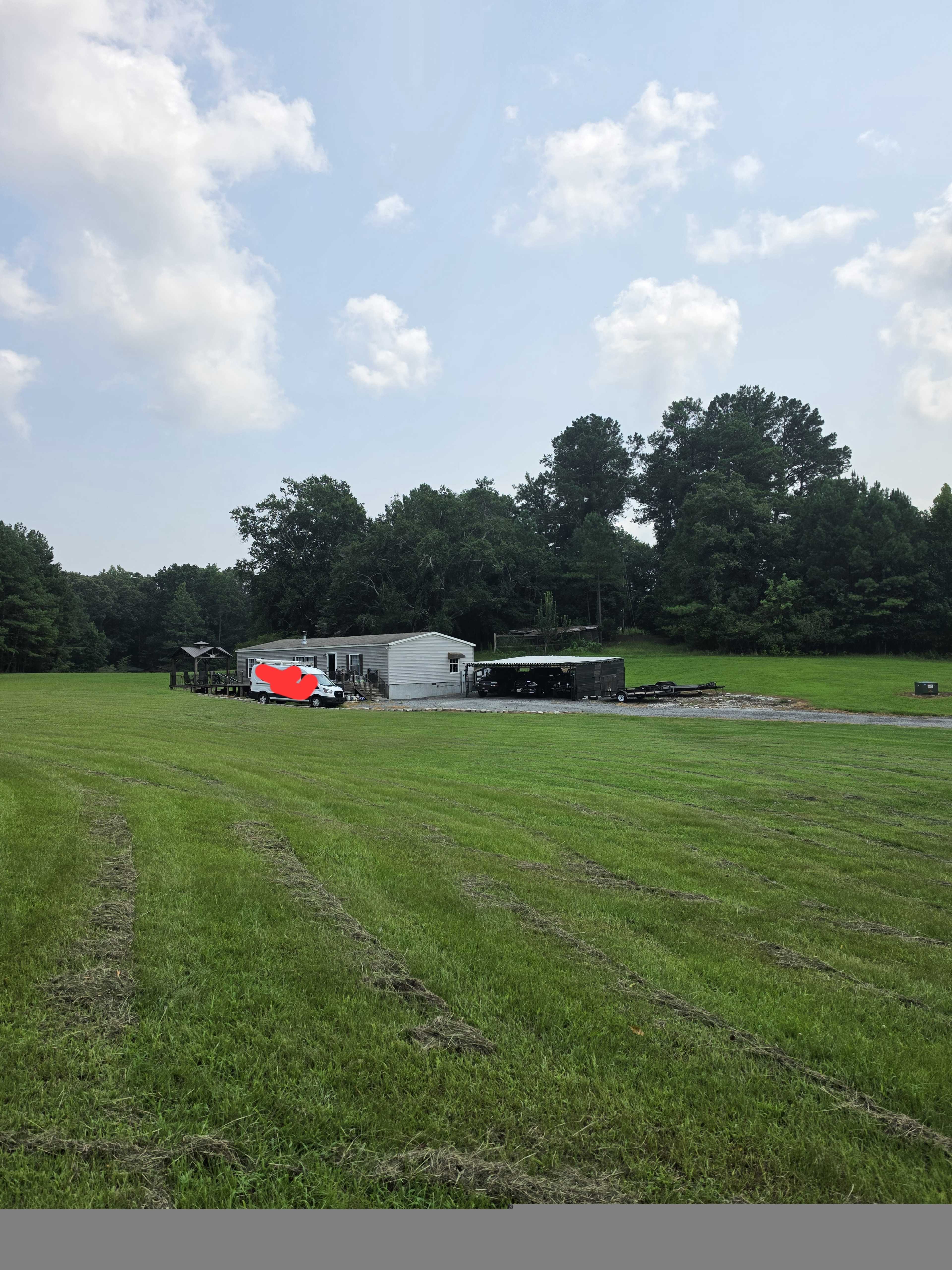 A single-story structure is situated in a grassy field, surrounded by trees under a partly cloudy sky.