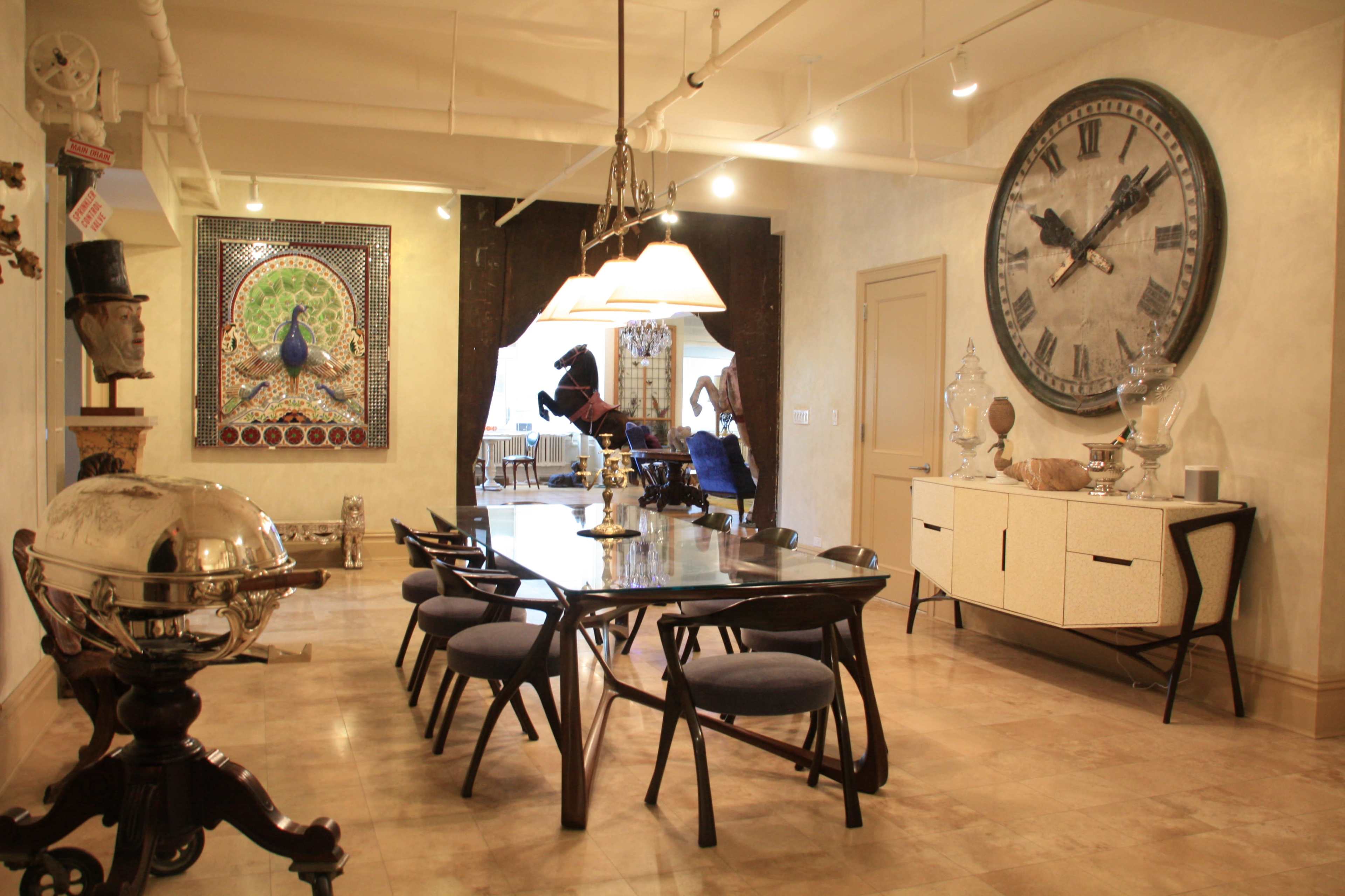 A dining room features a large table surrounded by chairs, a decorative wall clock, and various artwork and sculptures.