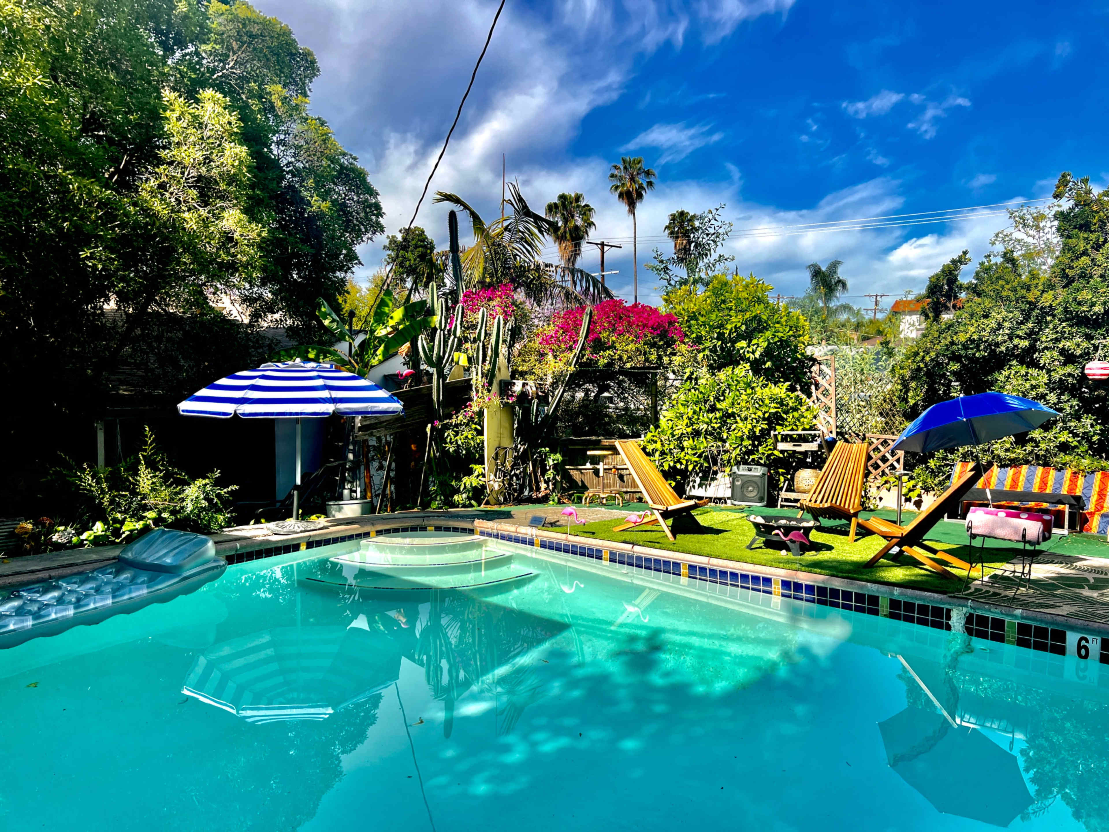 A vibrant outdoor pool area surrounded by lush greenery, with lounge chairs and umbrellas placed around the water.