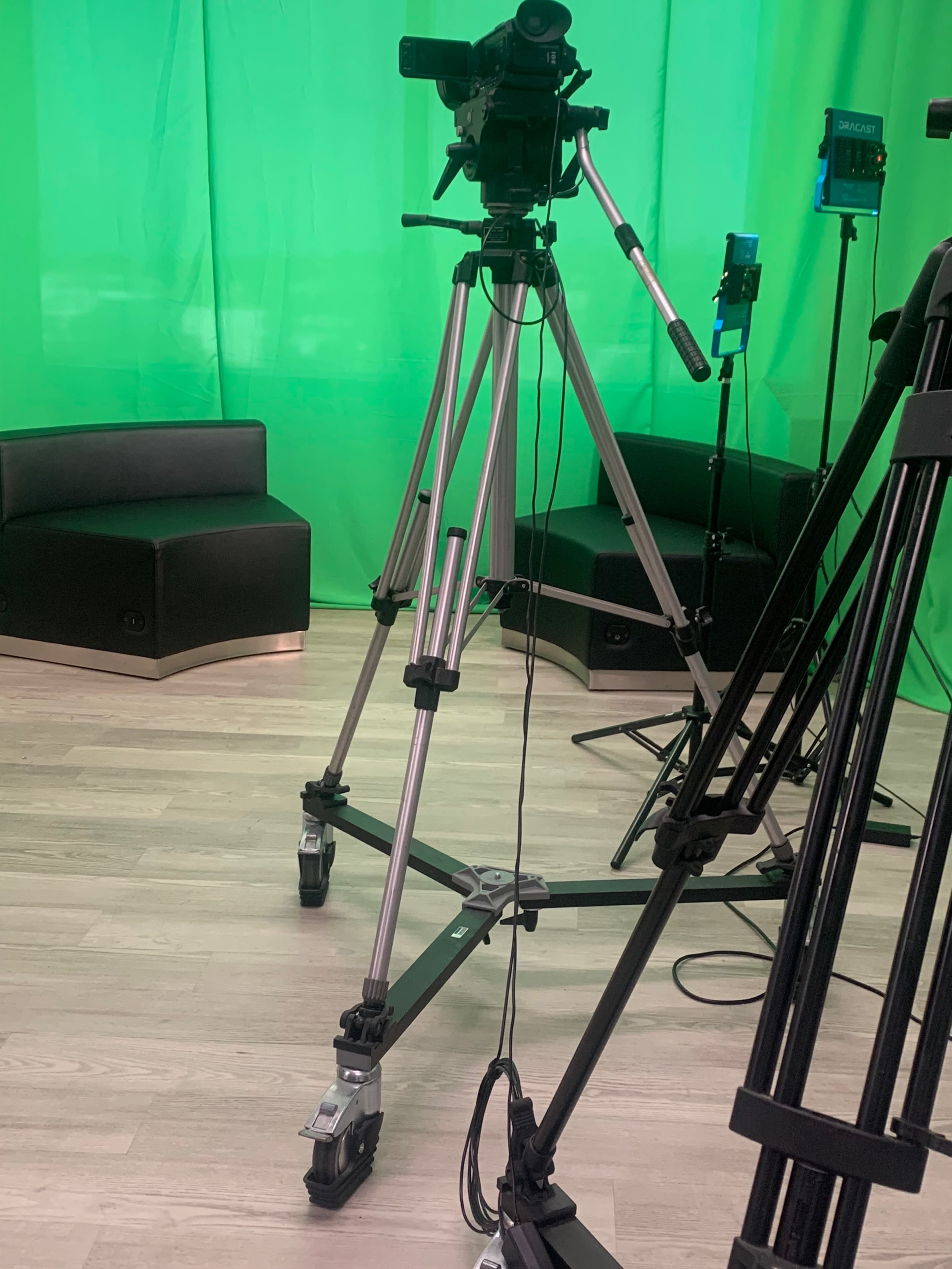 The image shows camera equipment set up in front of a green backdrop in a studio environment.