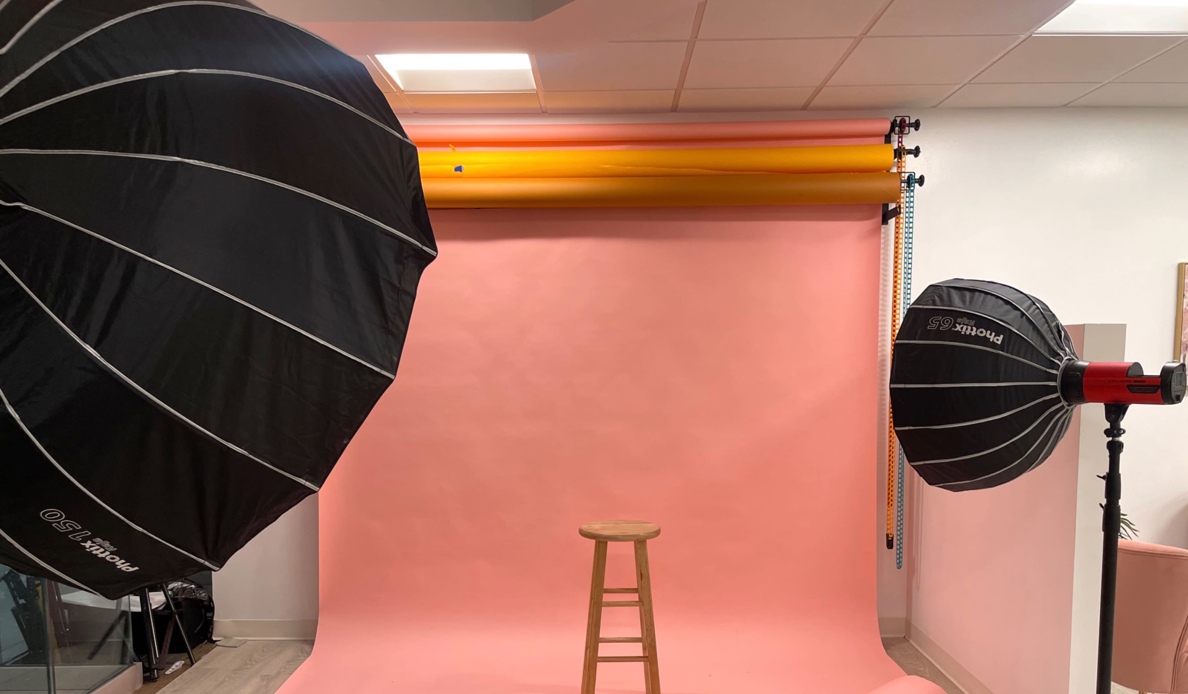 A photography studio setup with two large softboxes, a pink backdrop, and a wooden stool in the center.