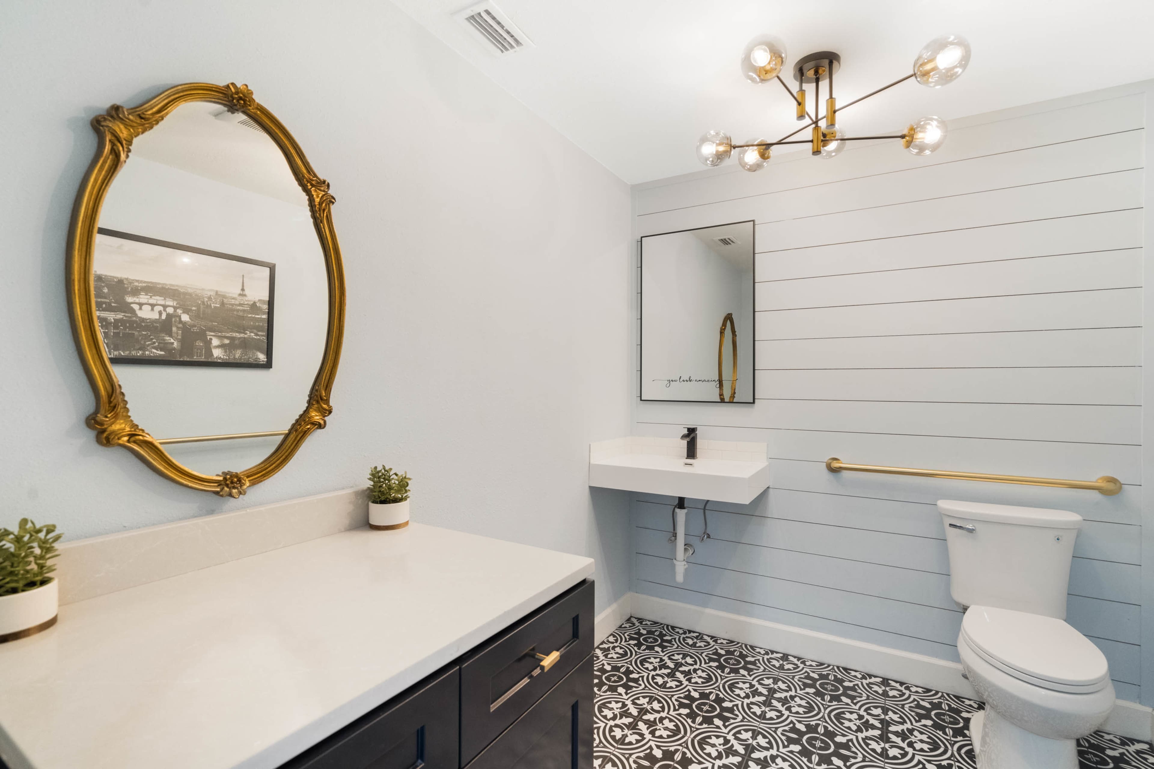 A modern bathroom features a wall-mounted sink, a toilet, and decorative elements like a mirror and light fixture against a paneled wall.