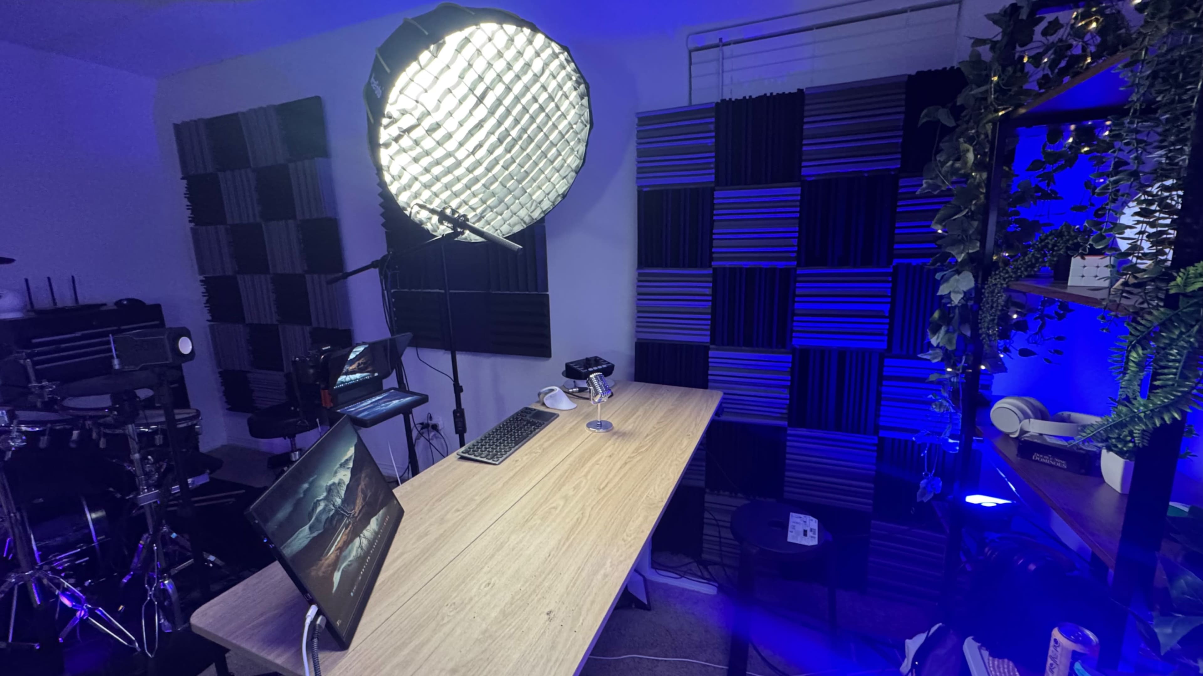 The image shows a modern workspace featuring a wooden desk with a laptop, a large softbox light, and sound-absorbing panels on the walls, illuminated by blue light.