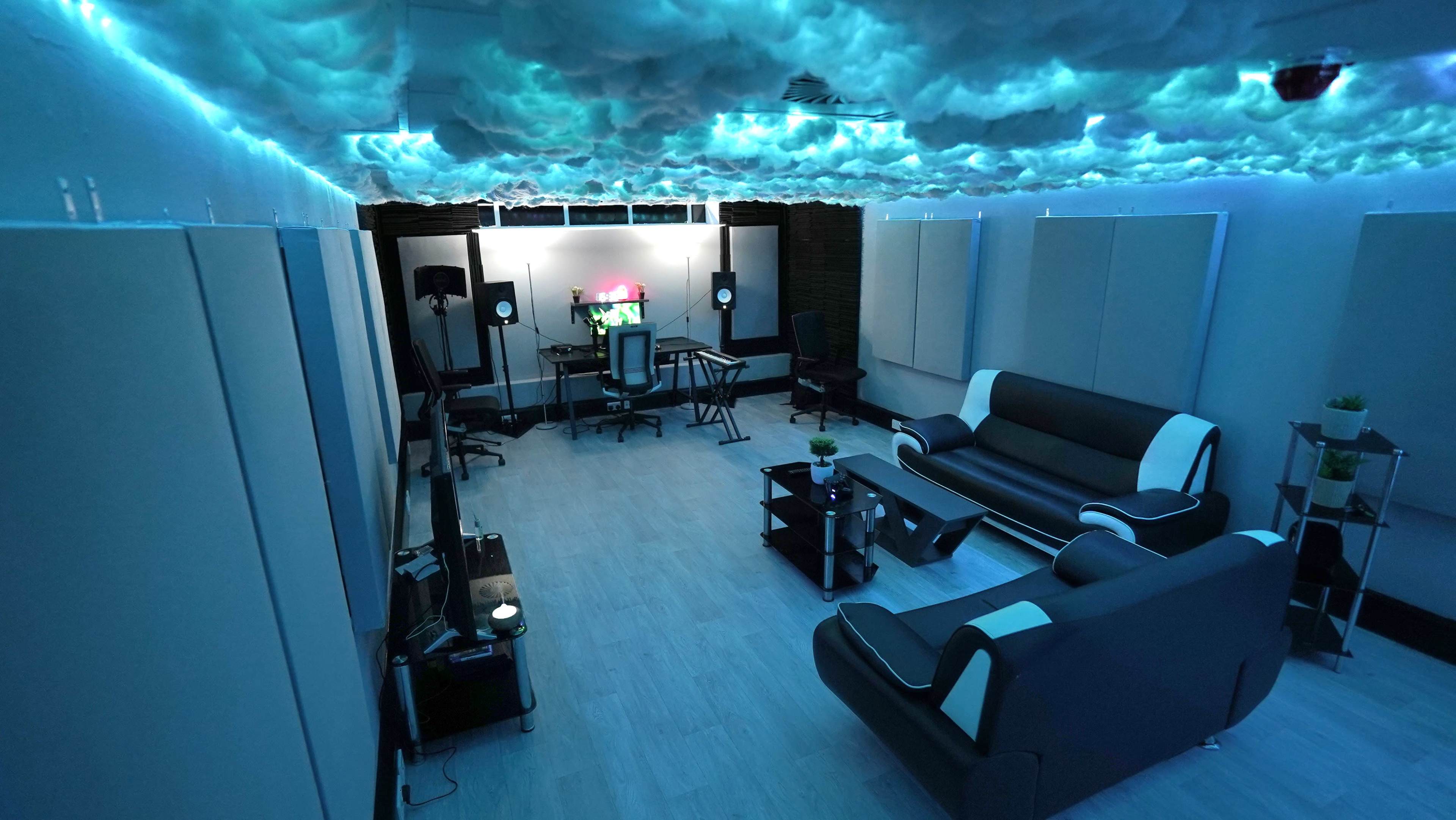 A modern studio room with a cloud-themed ceiling, comfortable seating, and sound equipment set up against the walls.
