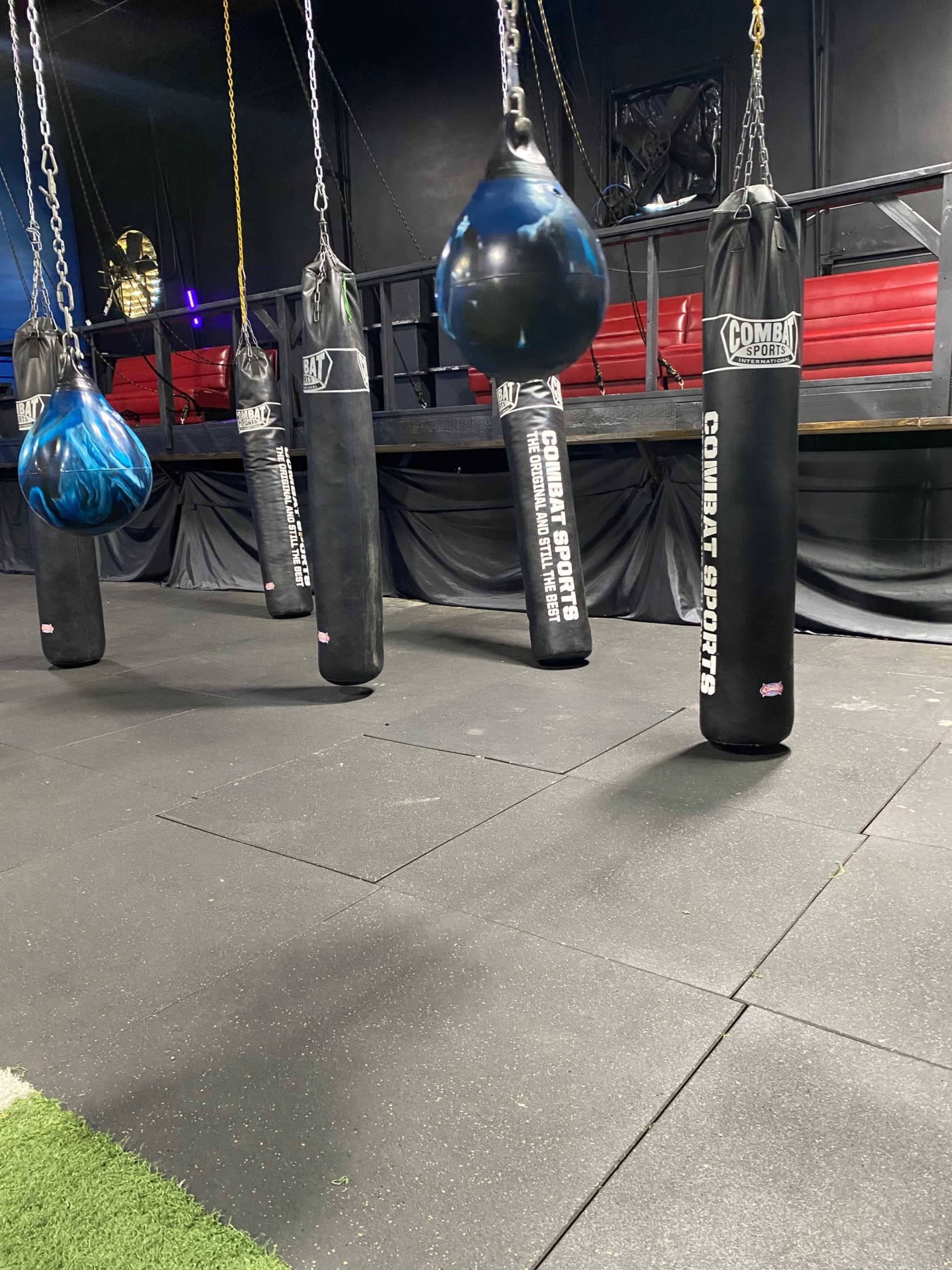 A row of heavy punching bags hanging from the ceiling in a gym setting.