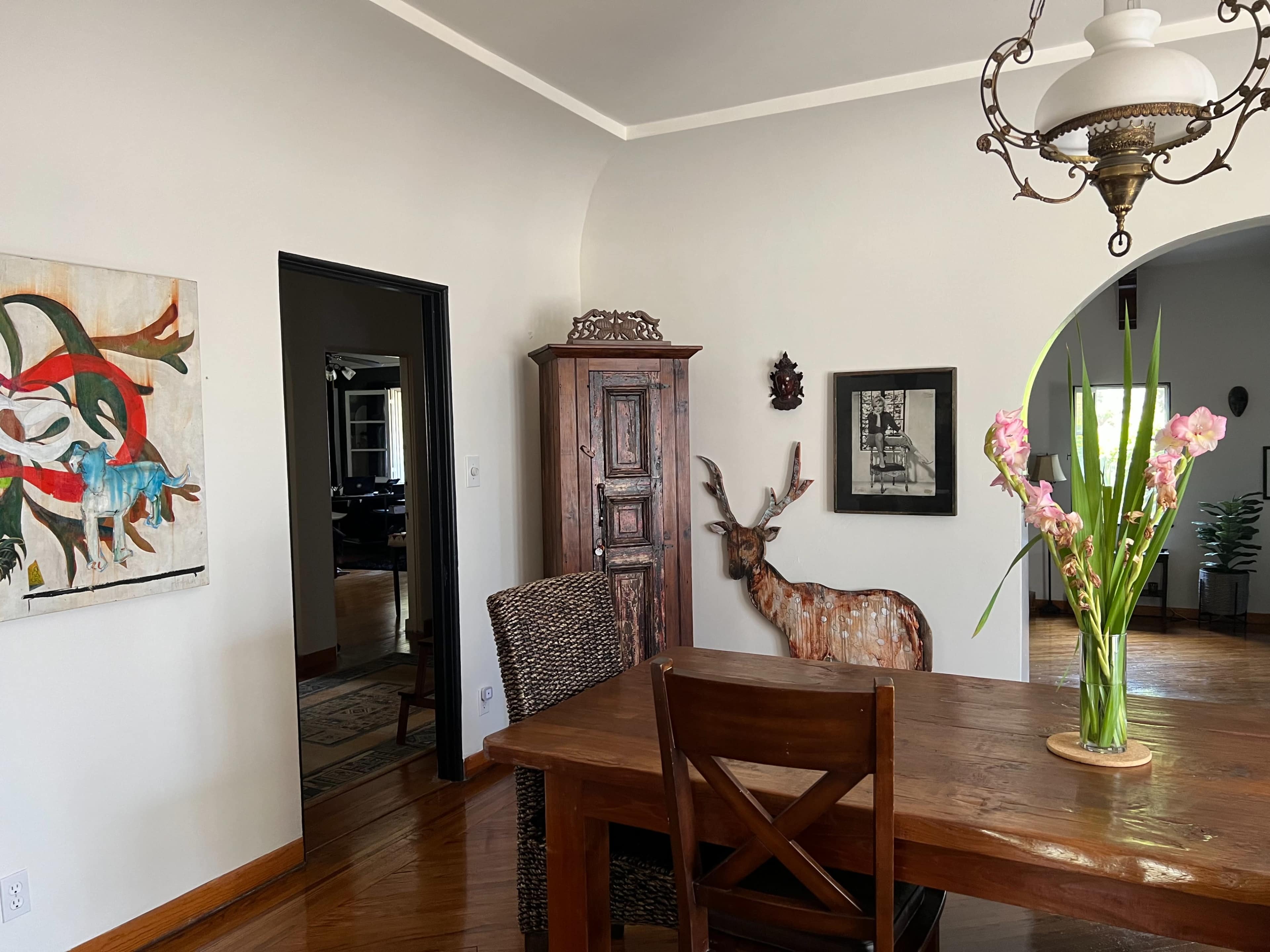 A dining area features a wooden table and chairs, a decorative deer statue, and a large painting on the wall, with an entryway visible in the background.