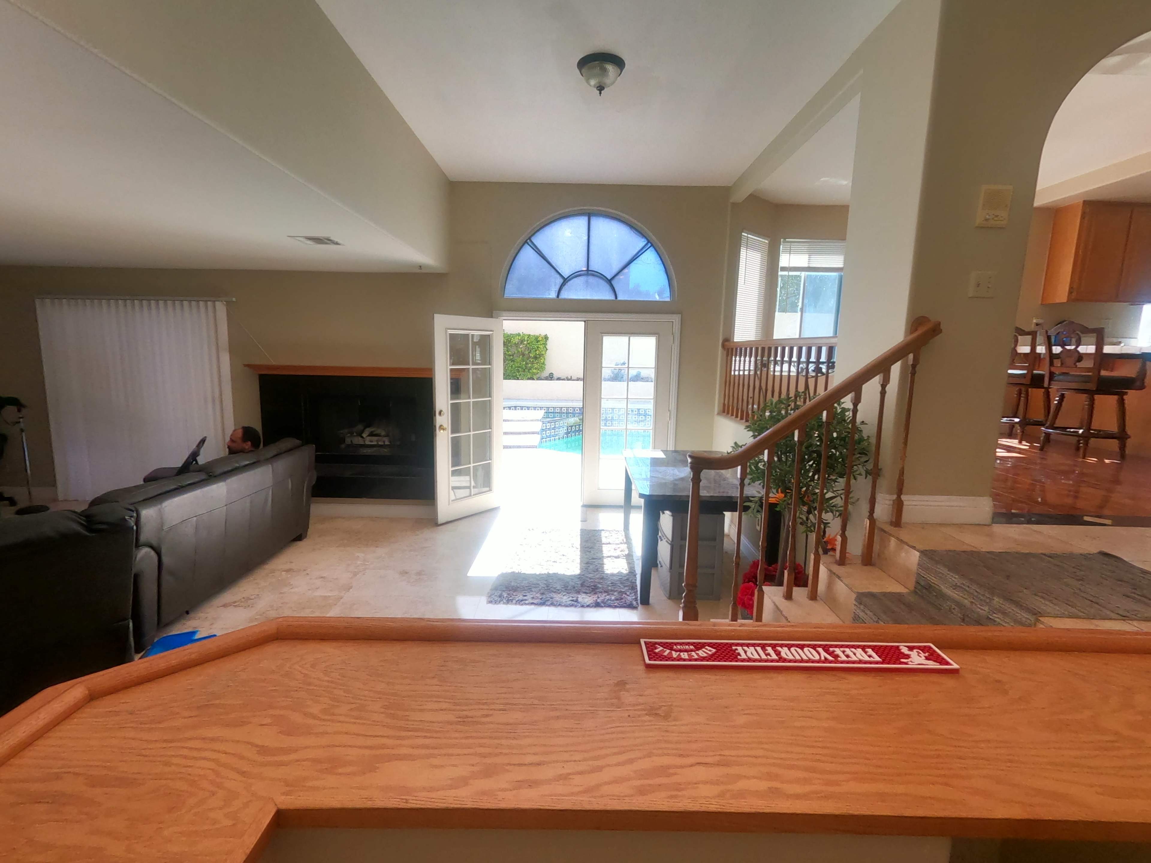 The image shows a spacious living room with a view of a pool area through large glass doors, featuring a staircase leading down to the main floor.