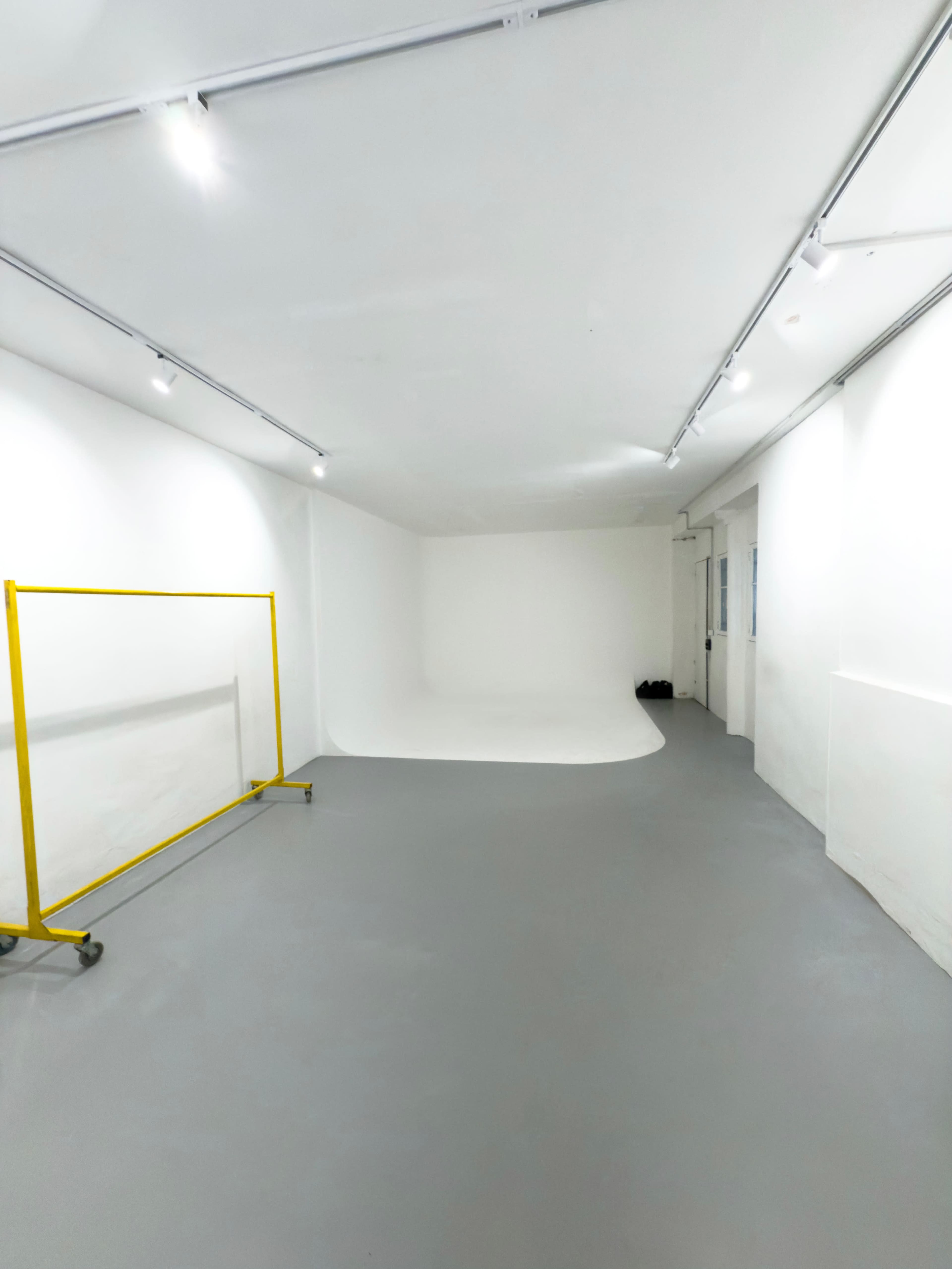 The image shows a spacious, well-lit photography studio with a white backdrop and a yellow frame on wheels in the foreground.