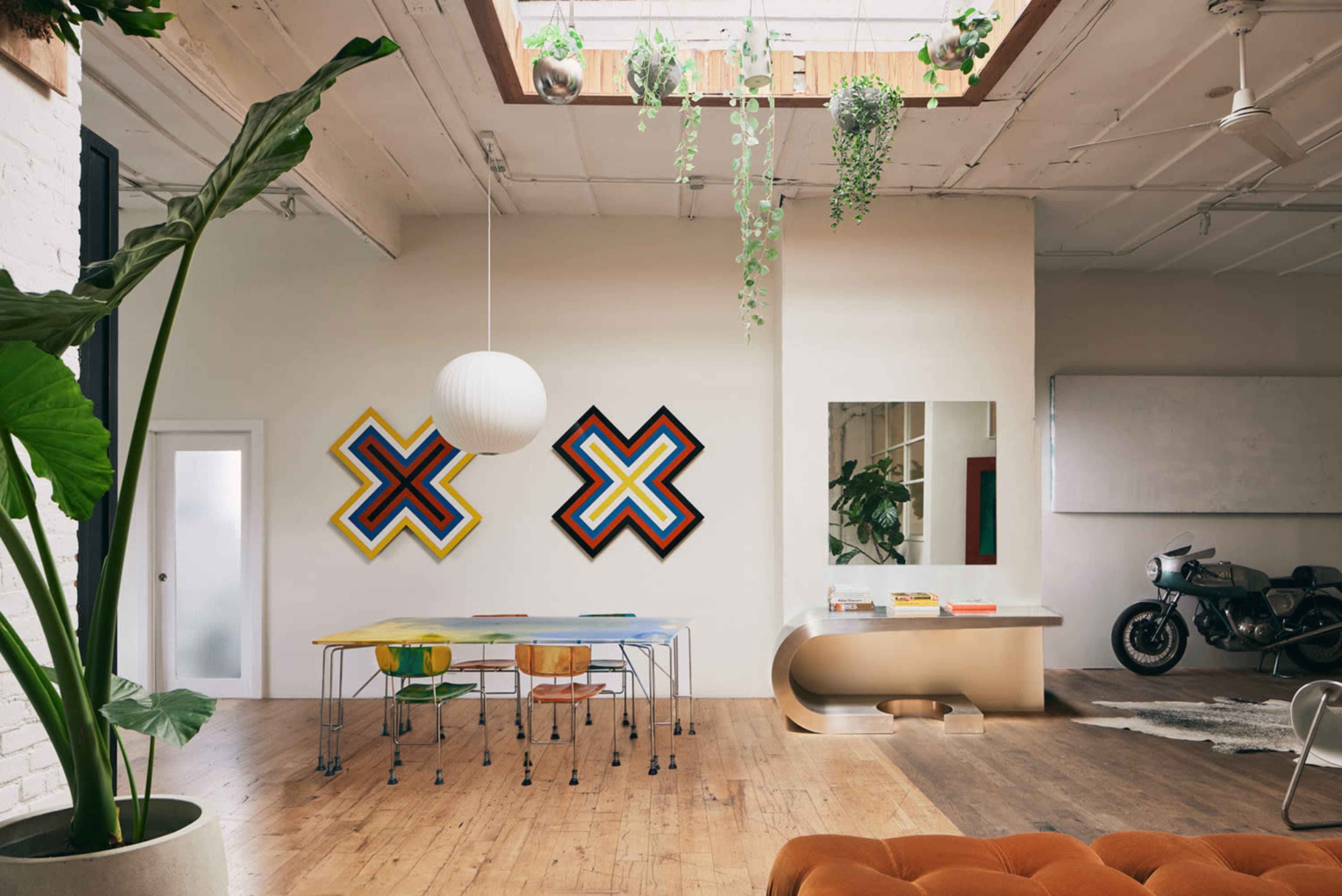 A spacious interior with a dining area featuring colorful artwork on the walls, a reflective mirror, and a motorcycle in the corner.