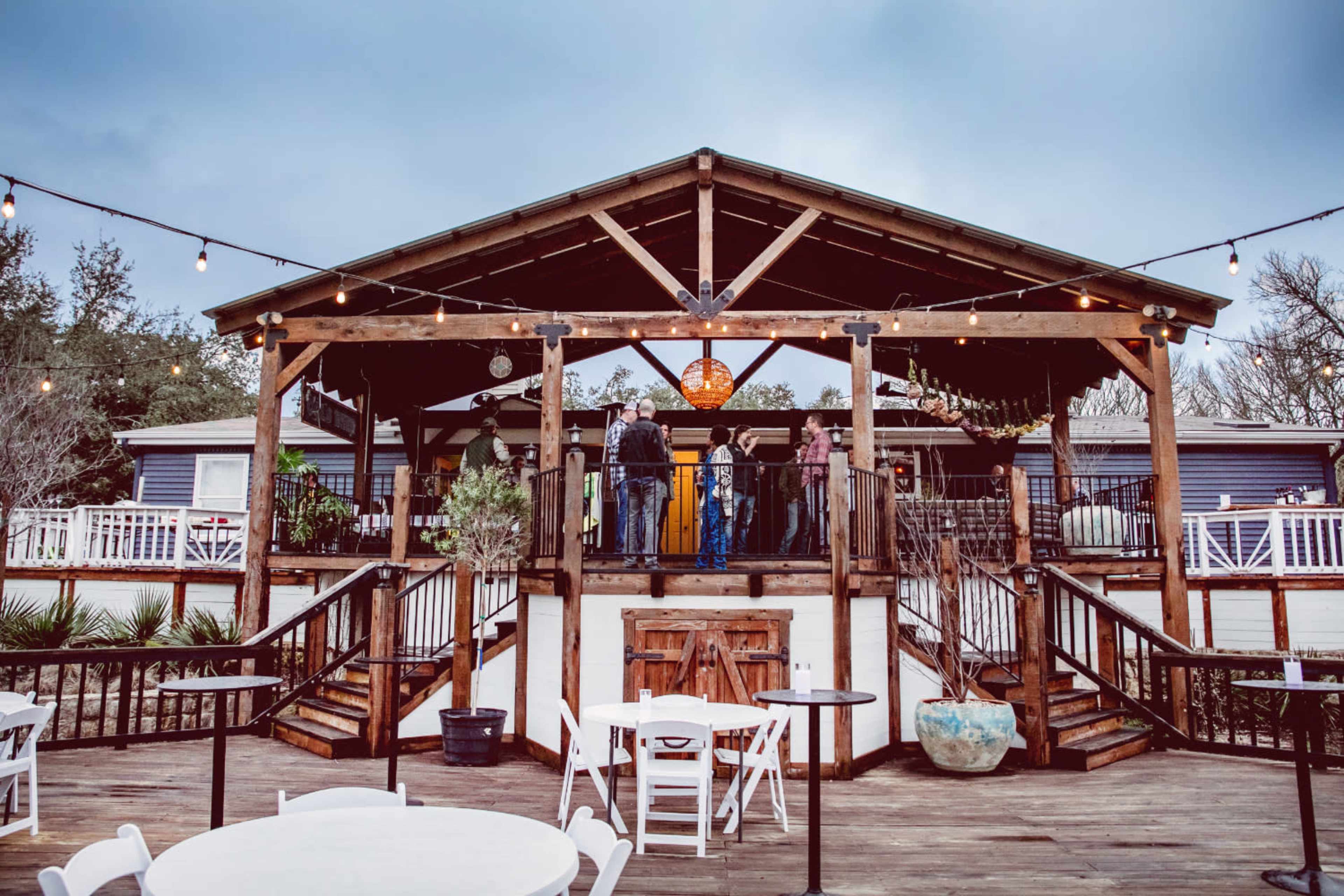 A wooden pavilion with string lights hosts a group of people gathered on a deck overlooking the entrance.