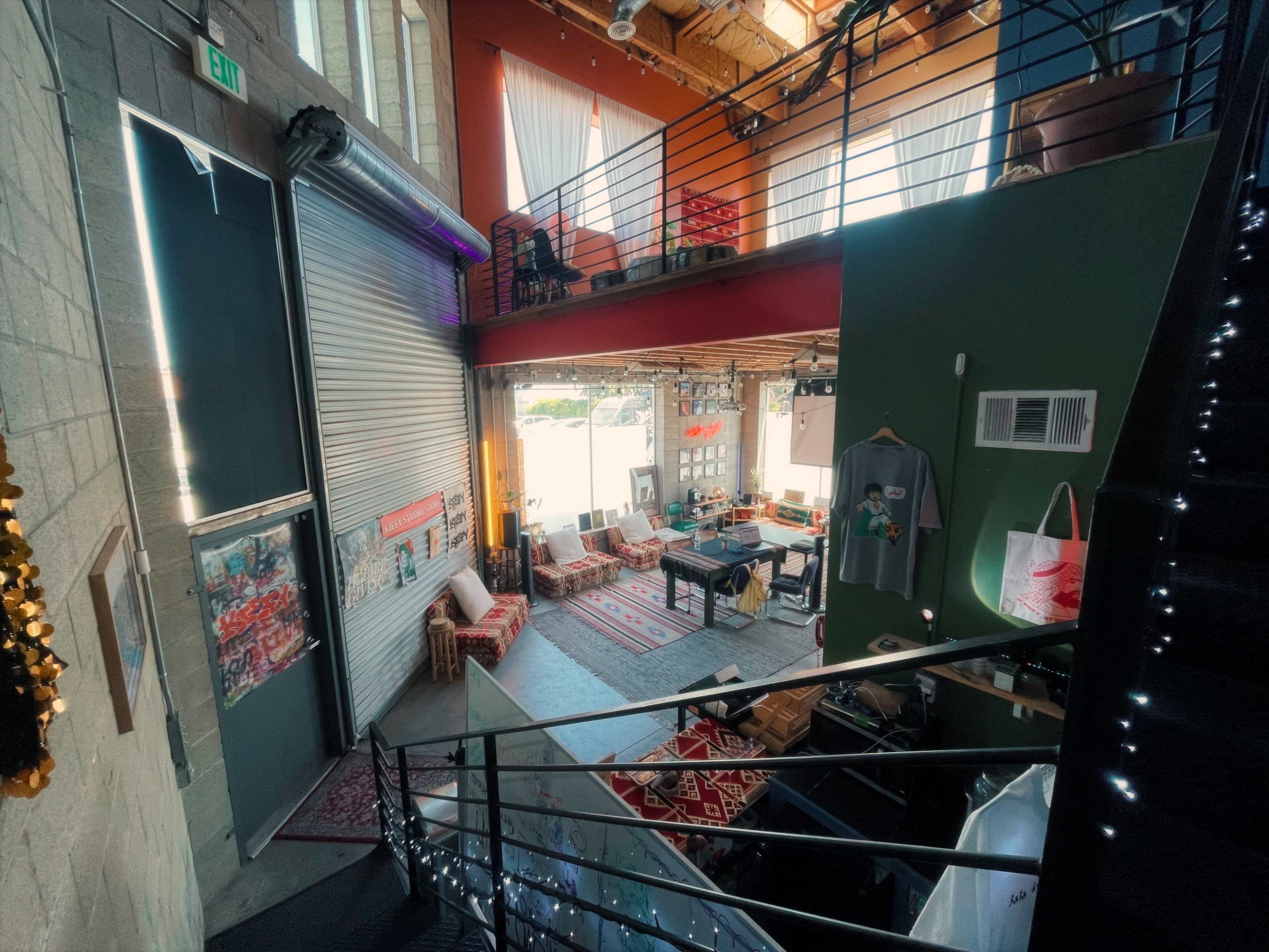 The image shows an indoor space with two levels featuring a staircase, colorful walls, seating areas, and large windows allowing natural light.