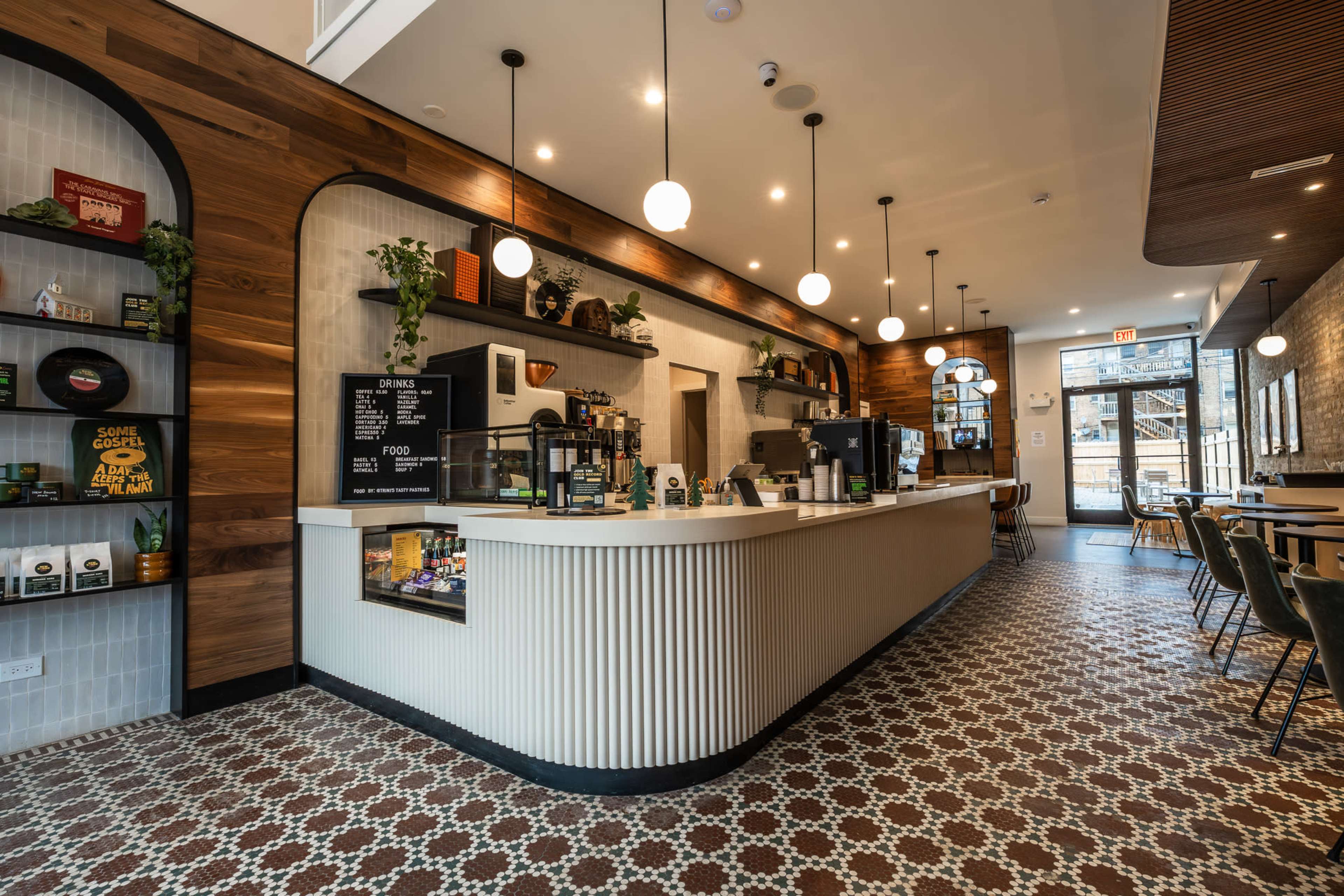 The image shows a modern coffee shop interior featuring a long white counter, decorative wooden walls, and patterned tile flooring.