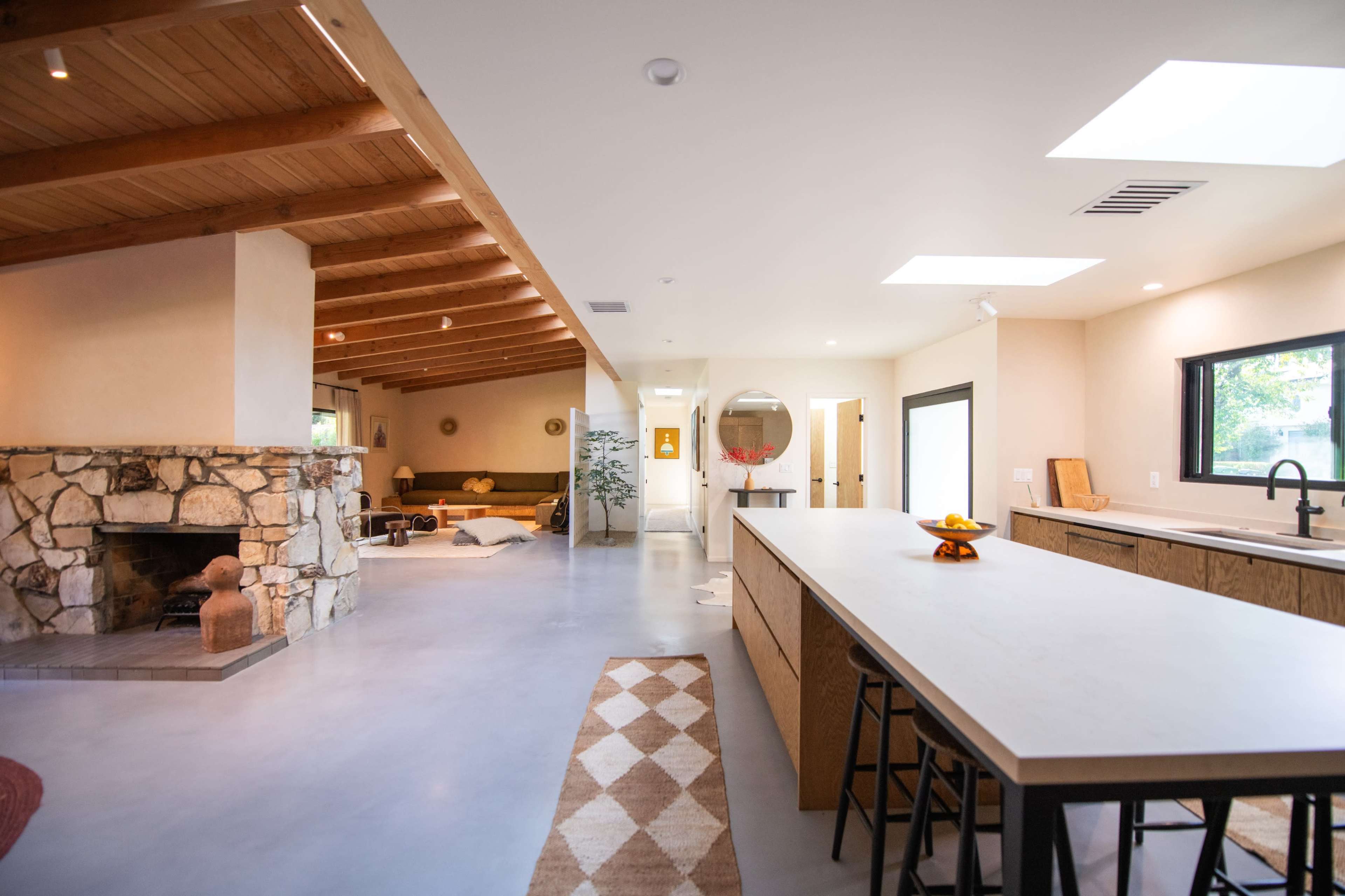 A modern interior features an open living space with a stone fireplace, kitchen island, and wooden beam ceiling.