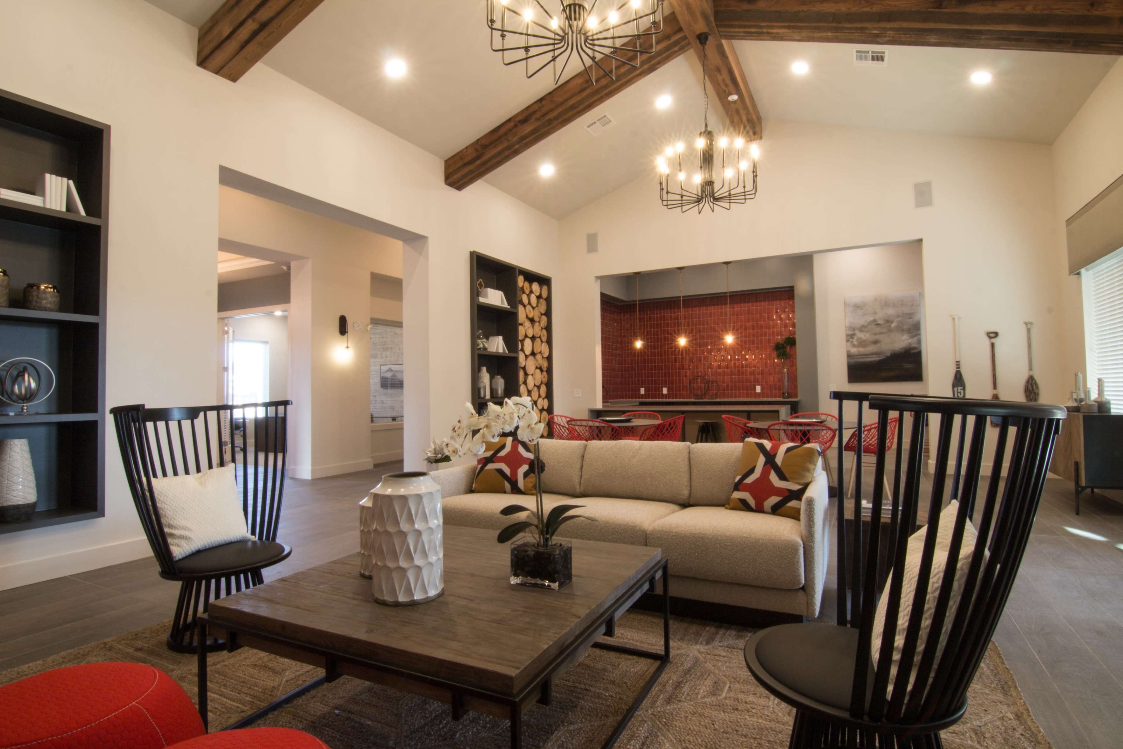 A modern living room with a high ceiling, wooden beam accents, a sectional sofa, and decorative lighting.