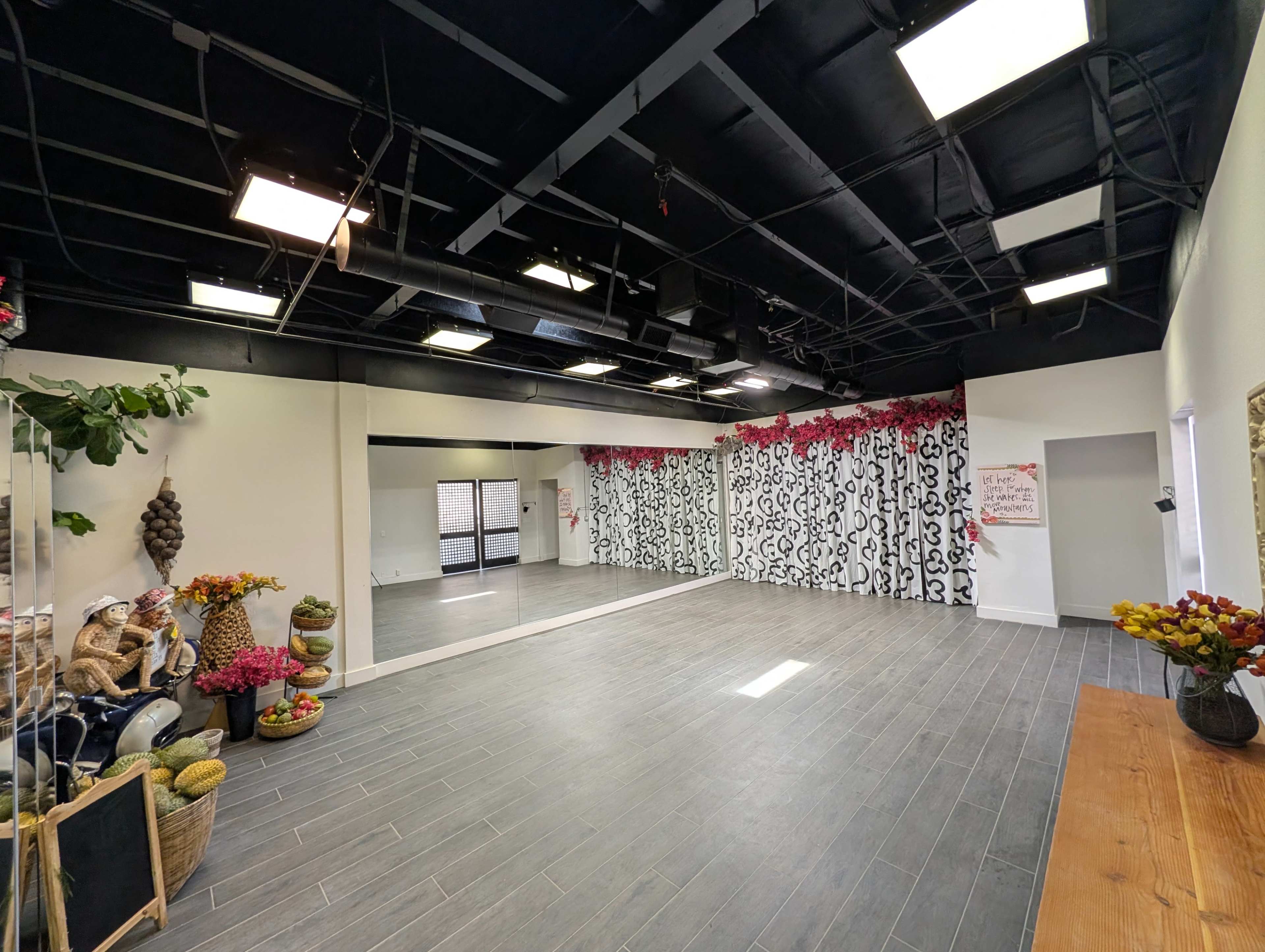 The image shows an empty dance studio with a large mirror, black and white patterned curtains, and floral decorations at one end.