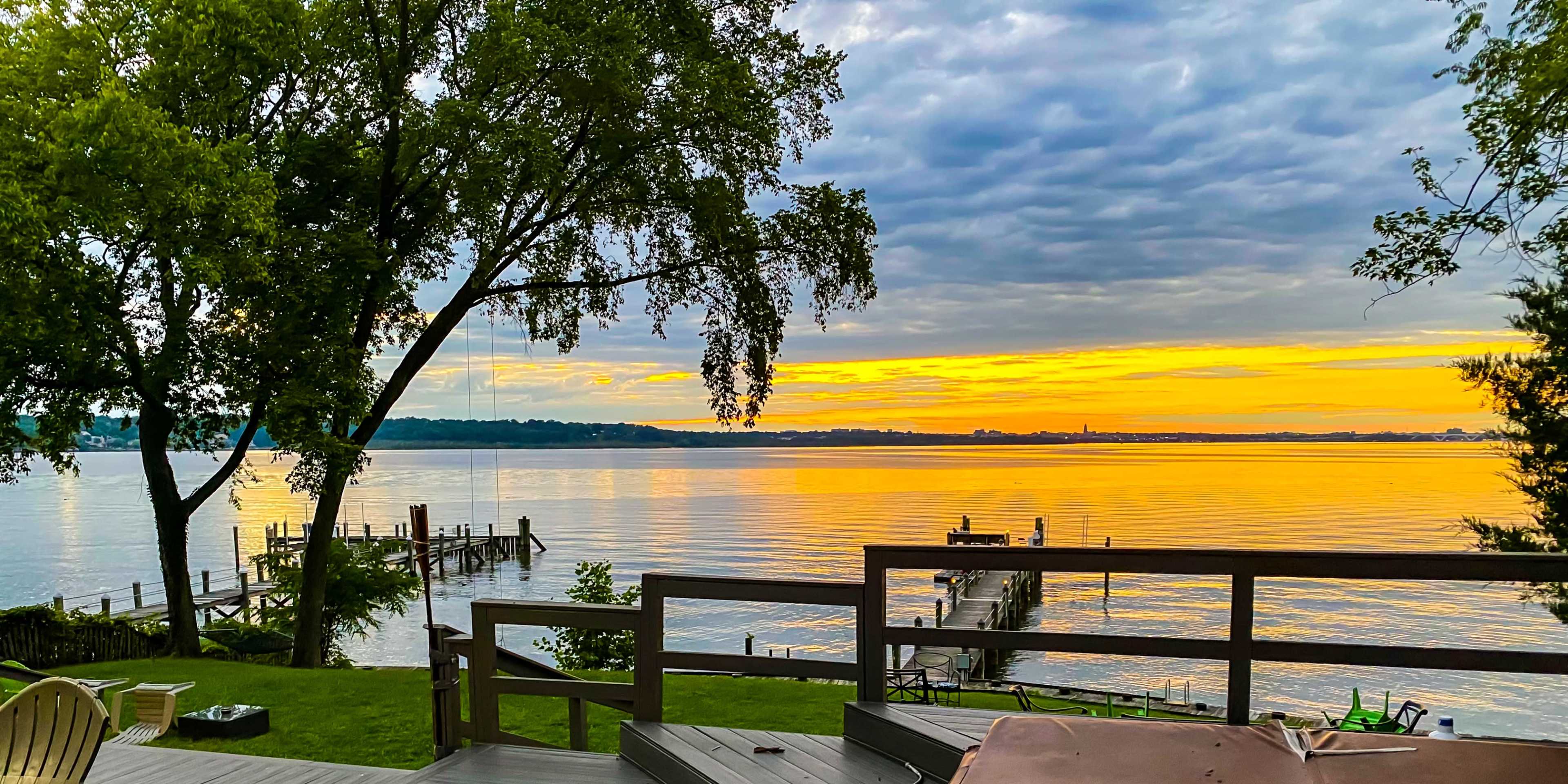 The image shows a calm lakeside scene at sunset, with a dock extending into the water and trees lining the shore.