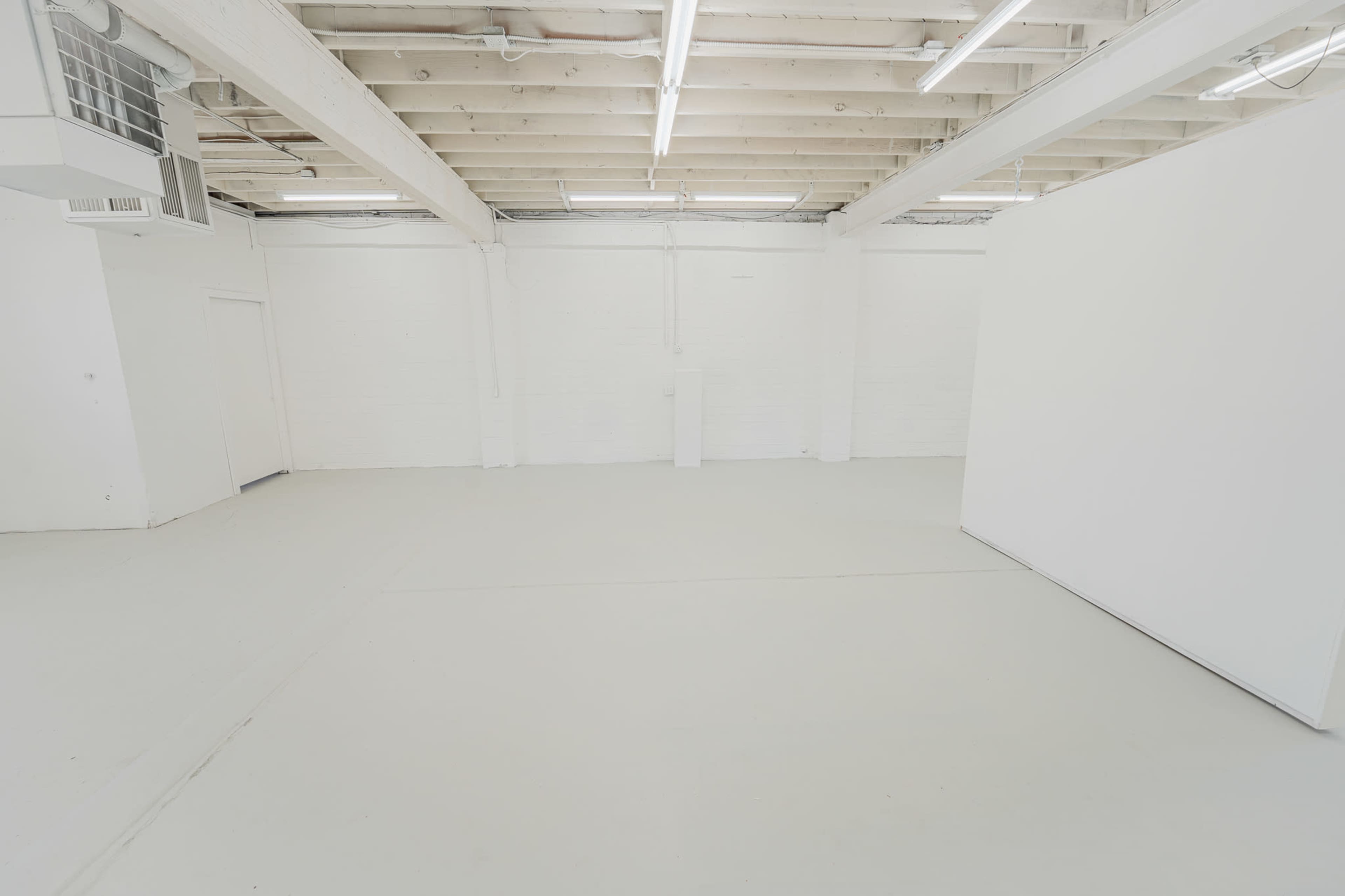 A spacious, empty room with white walls, a white floor, and overhead lights.