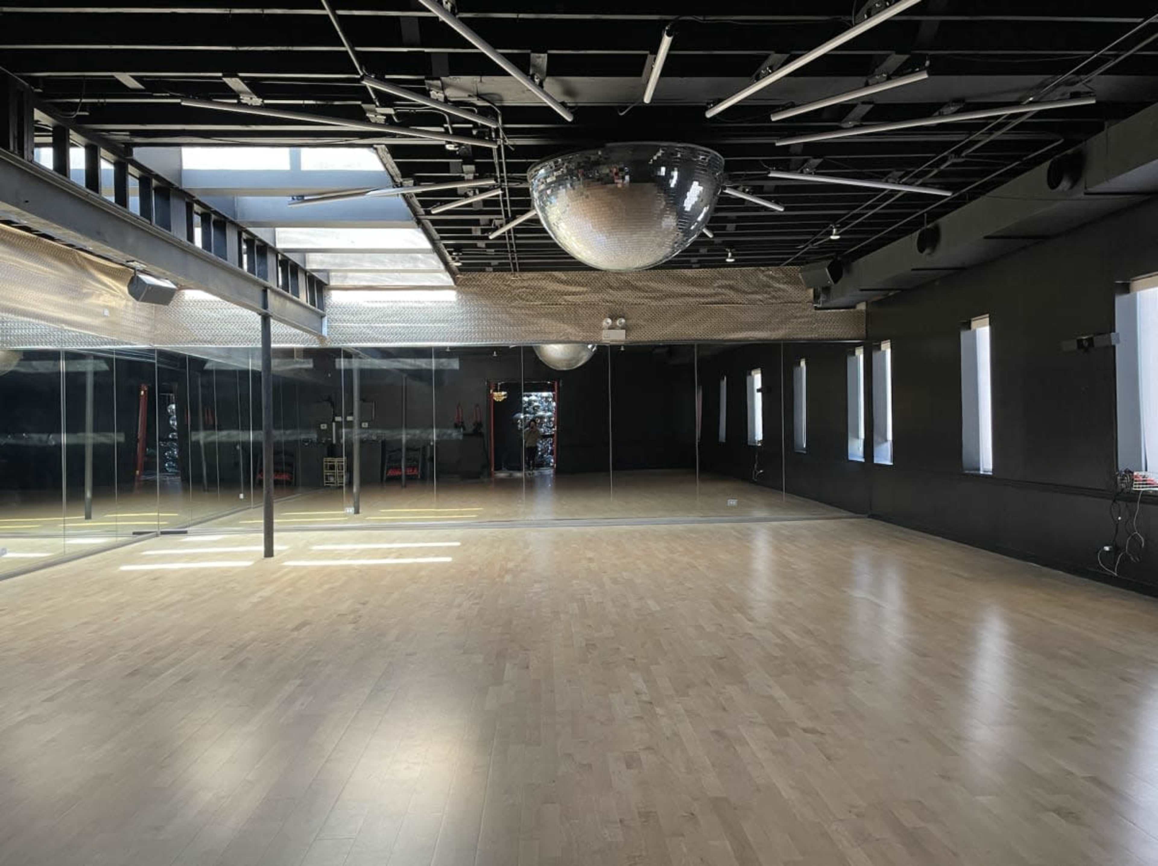 An empty dance studio with a large mirror wall, wooden floor, and a disco ball hanging from the ceiling.