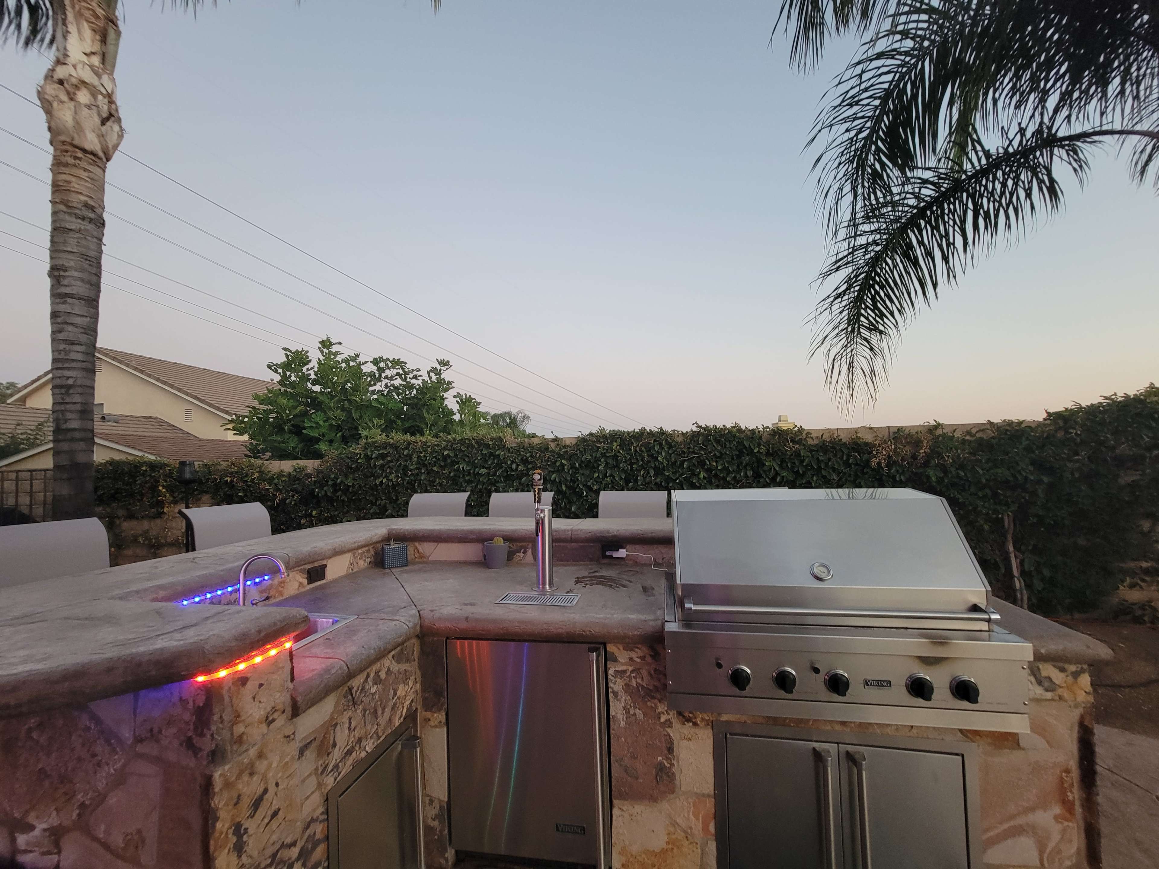 An outdoor kitchen with a stone countertop, an integrated grill, and a palm tree in the background.