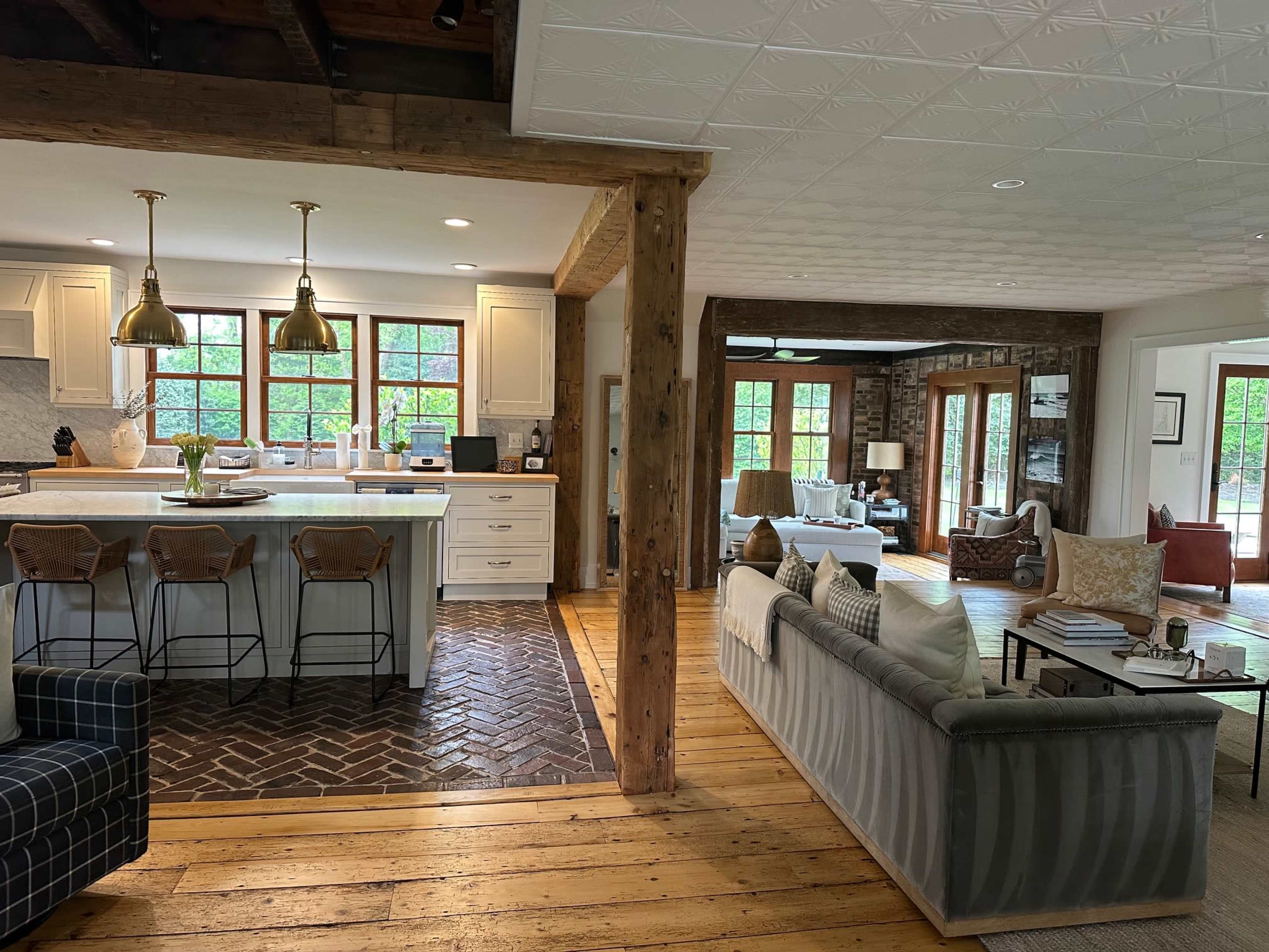 The image shows an open-concept living space featuring a kitchen with a large island and bar stools, a dining area with wooden beams, and a cozy living room with various seating arrangements.