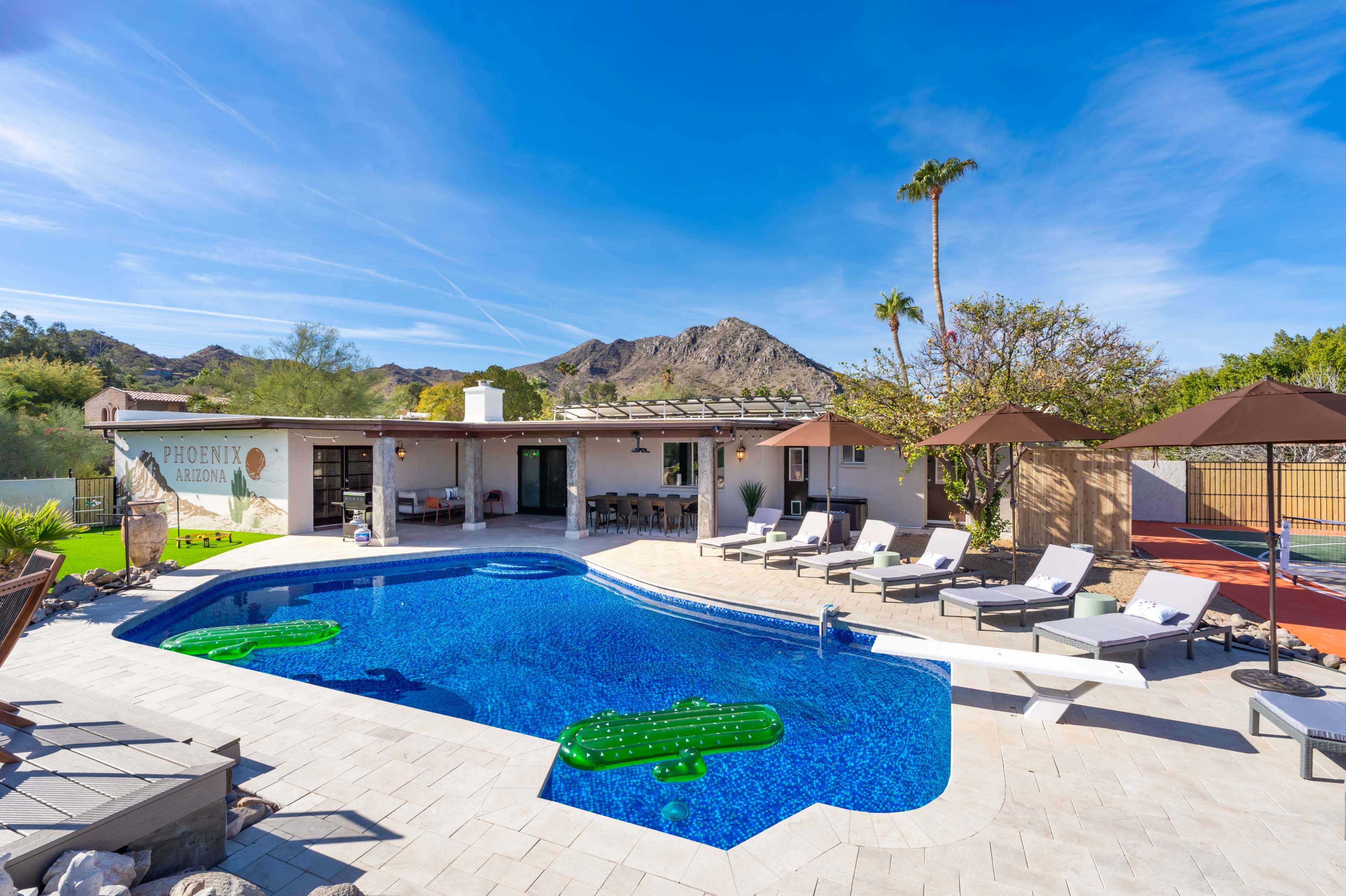 The image shows a backyard pool area with lounge chairs, umbrellas, and a view of mountains in the background.