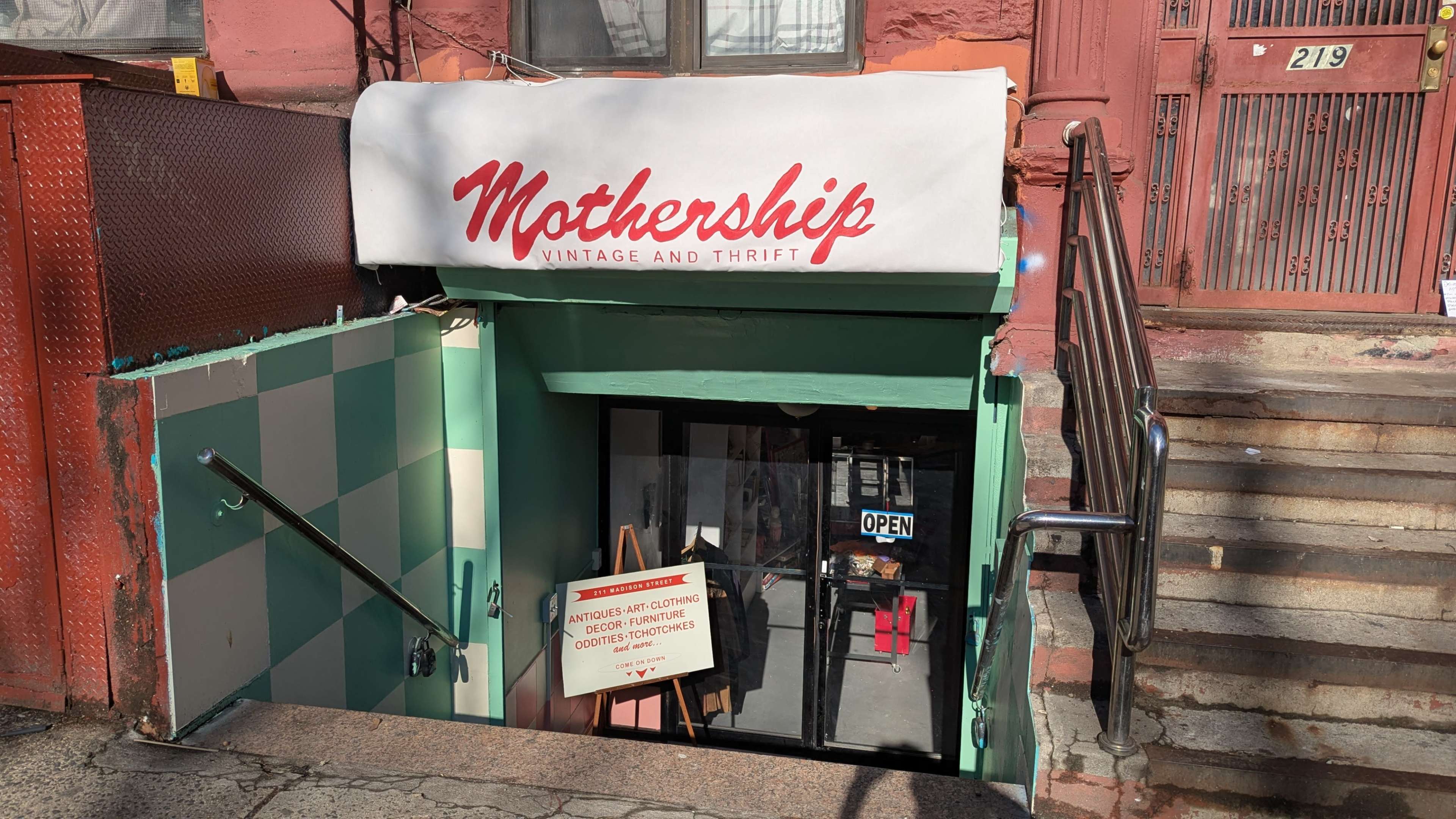 The image shows the entrance to "Mothership Vintage and Thrift," located below a staircase with an open sign visible in the window.
