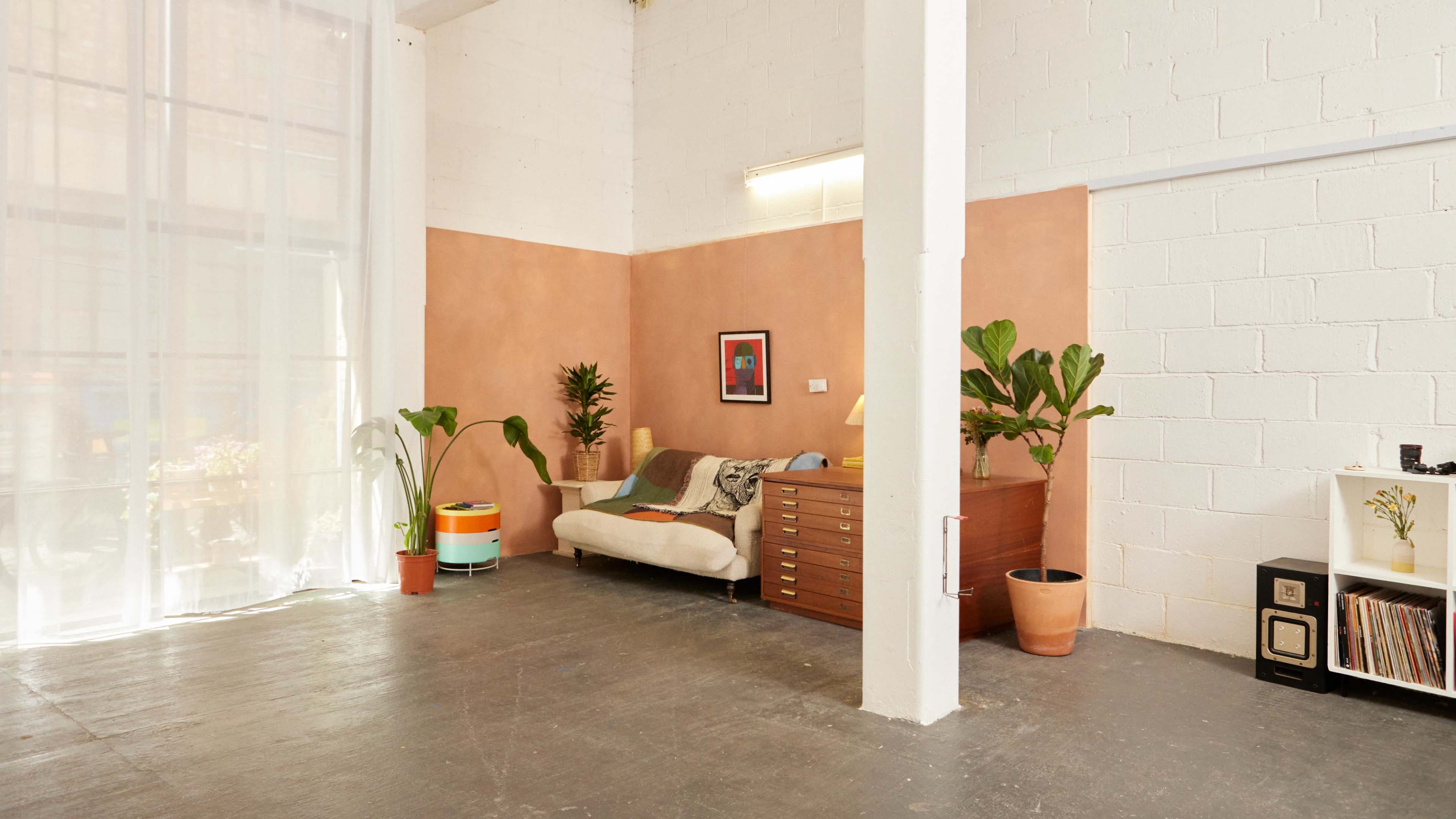 A spacious room with a beige couch, a wooden dresser, and several green plants against a textured wall.