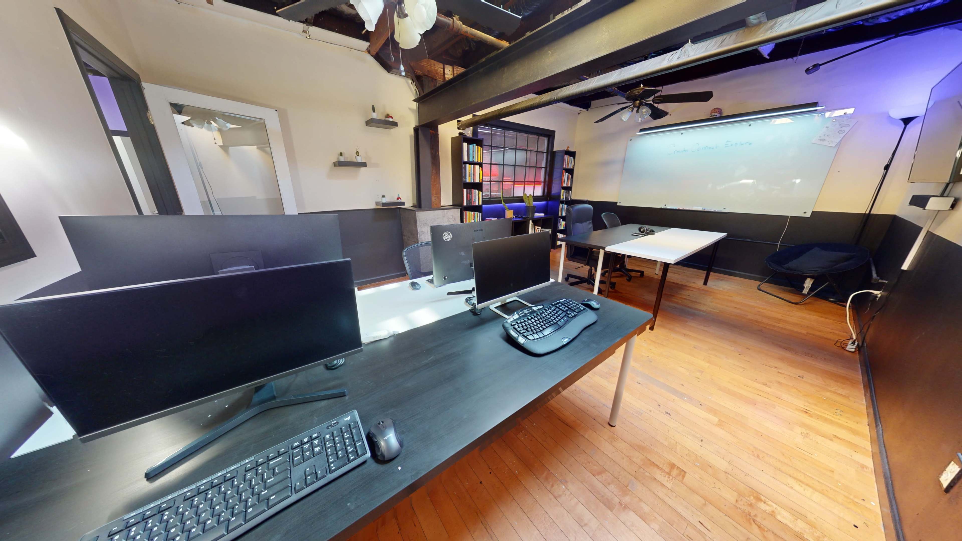 A modern office space with two large desks equipped with multiple monitors and keyboards, a whiteboard on the wall, and additional seating areas.