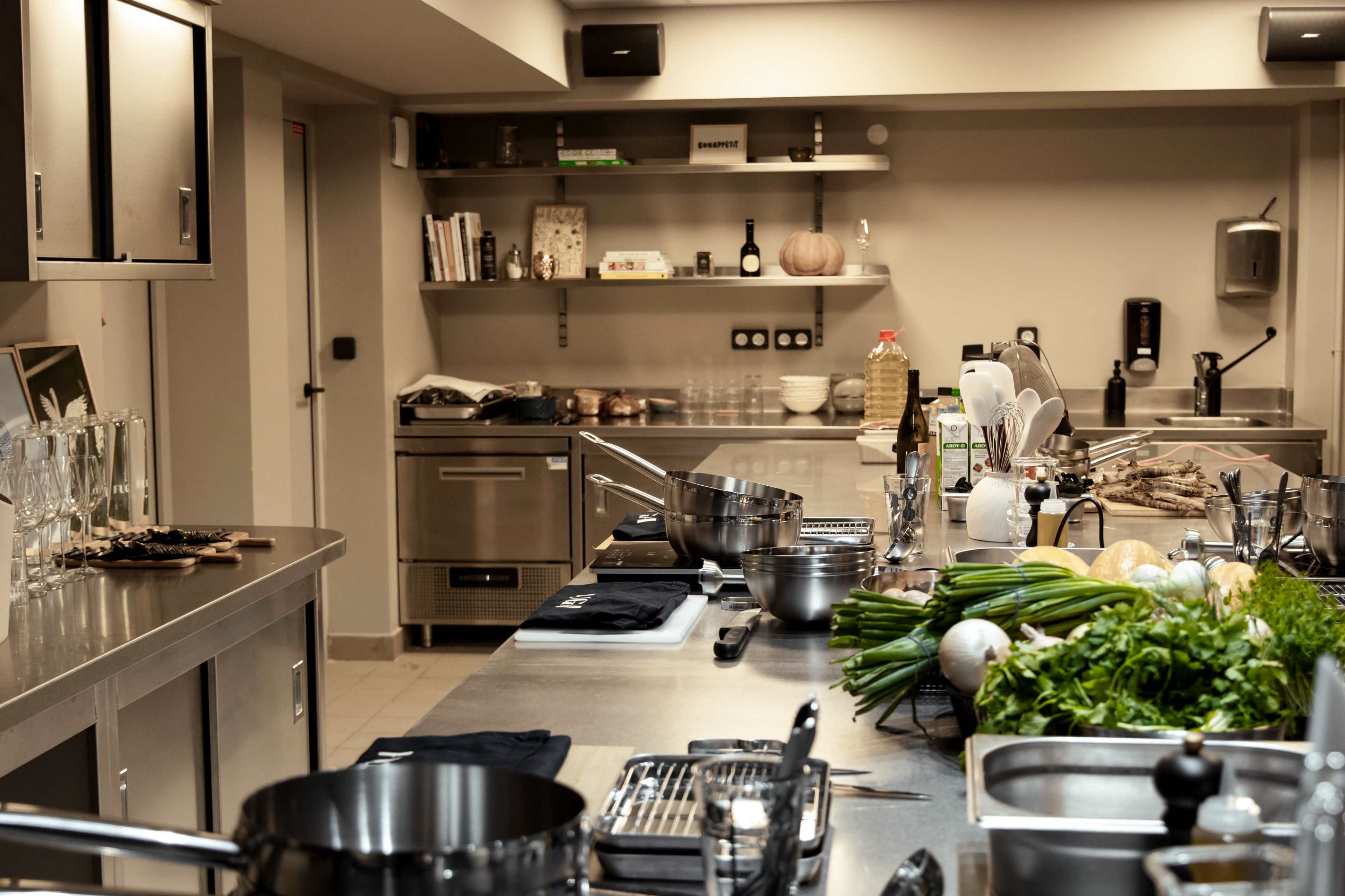 A modern kitchen workspace features stainless steel countertops, cooking equipment, and a variety of fresh ingredients neatly arranged on the counter.