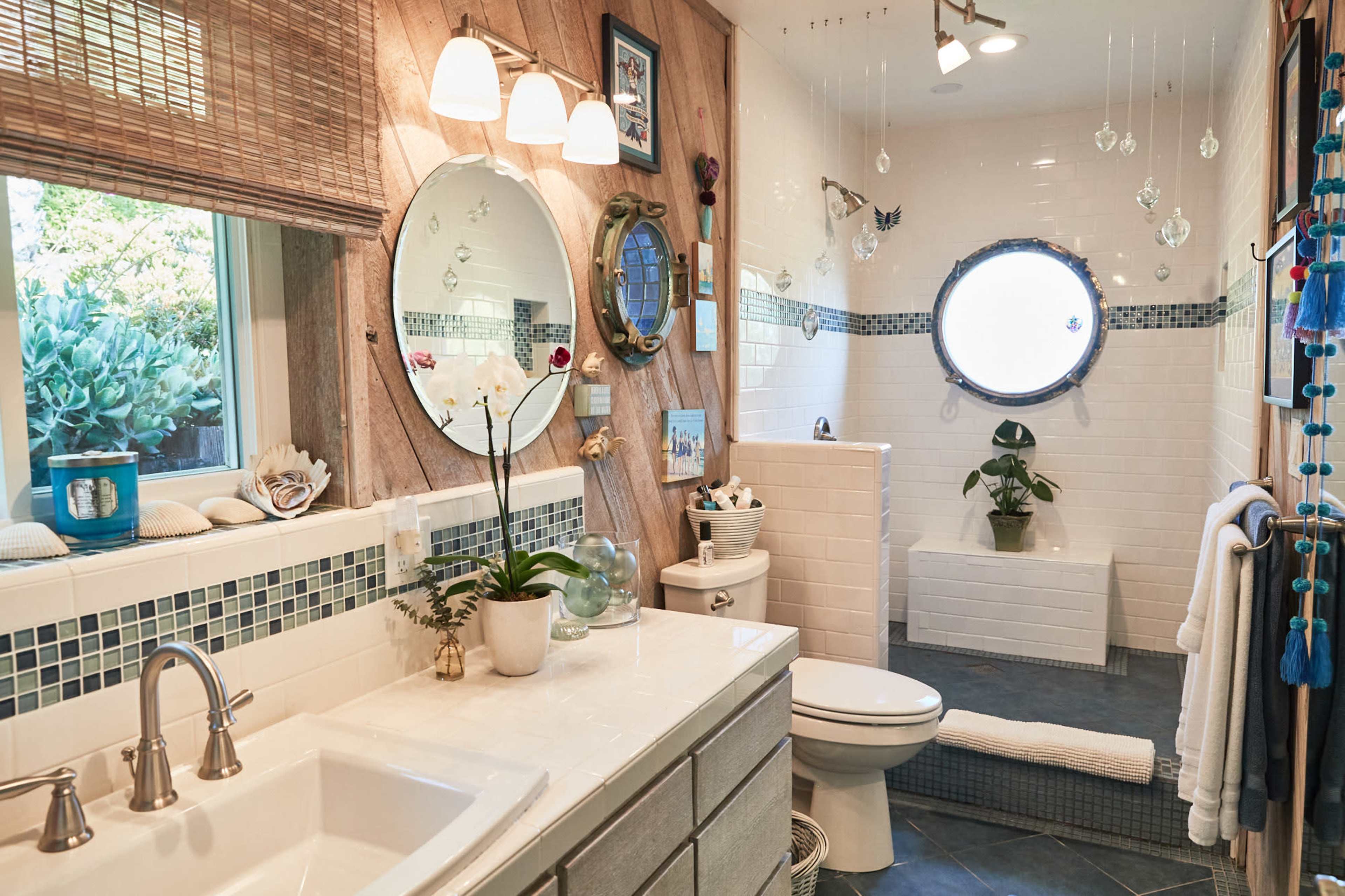 A bathroom features a white tile shower with a circular window, a double sink vanity, and various decorative elements on the walls.