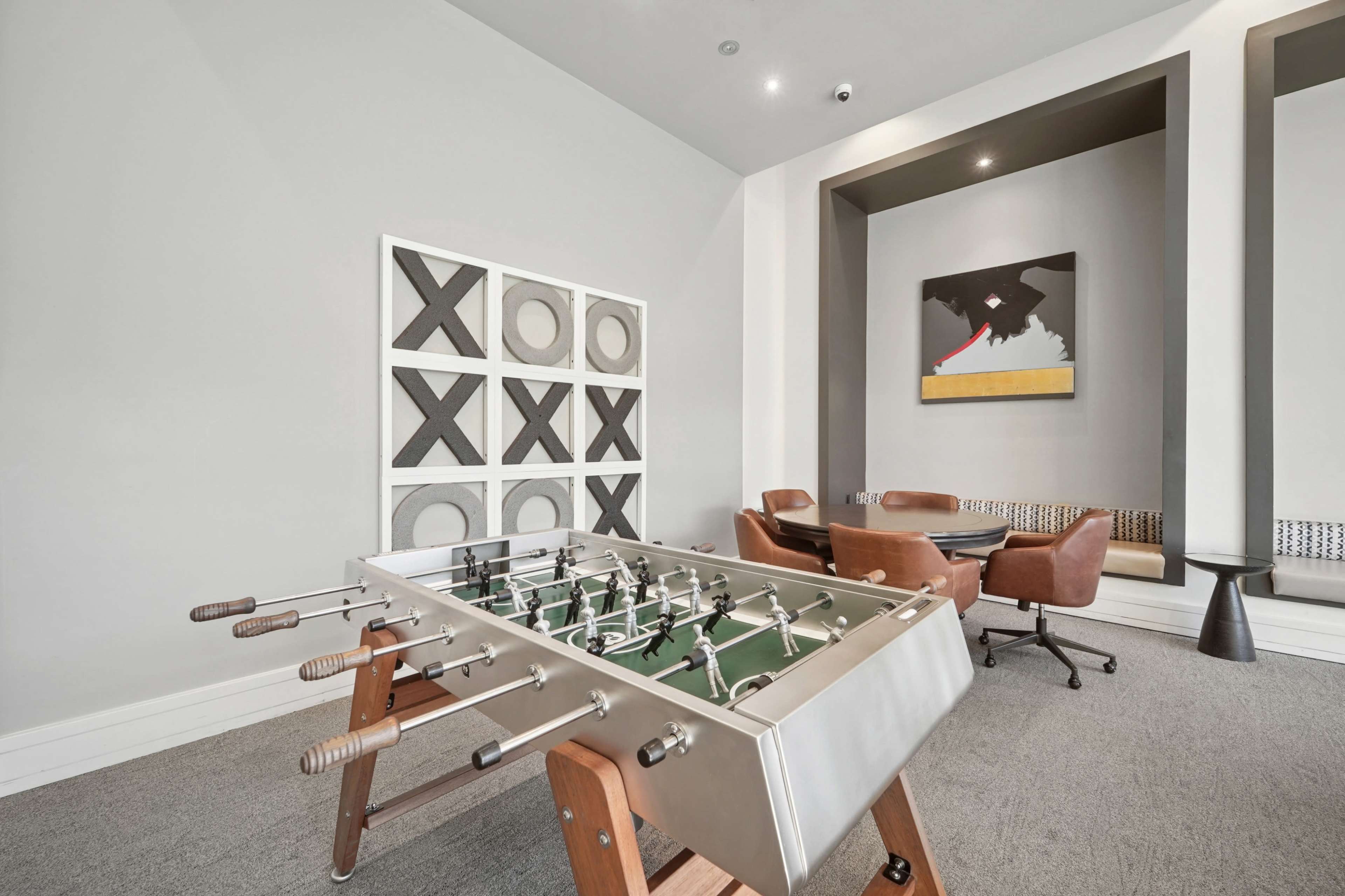 The image shows a modern lounge area featuring a foosball table, a large abstract art piece on the wall, and seating arrangements.