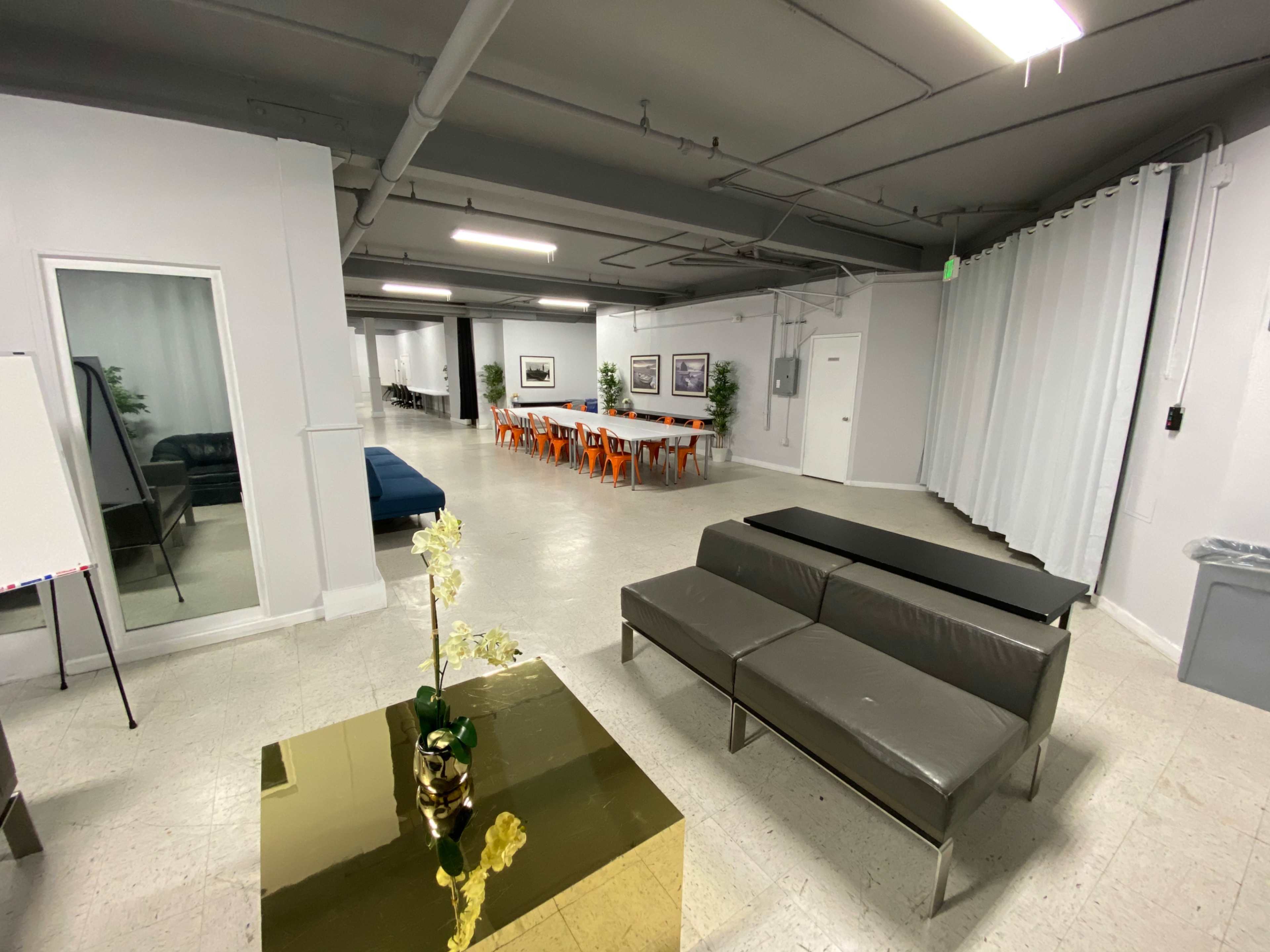 A modern interior space with a seating area, a conference table with chairs, and a partitioned section.