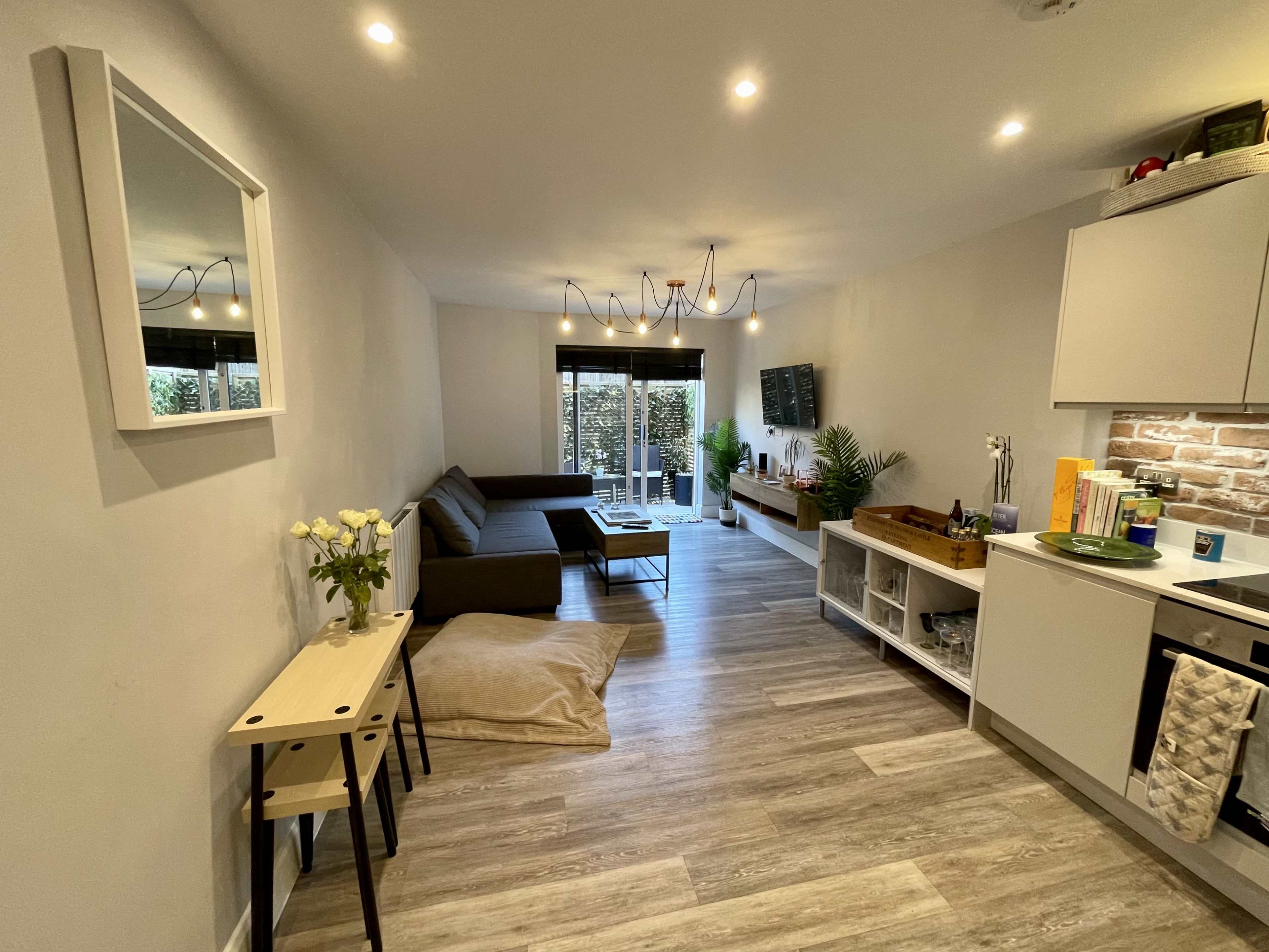 A modern living space with a gray sofa, a coffee table, a small kitchen area, and large windows leading to an outdoor area.