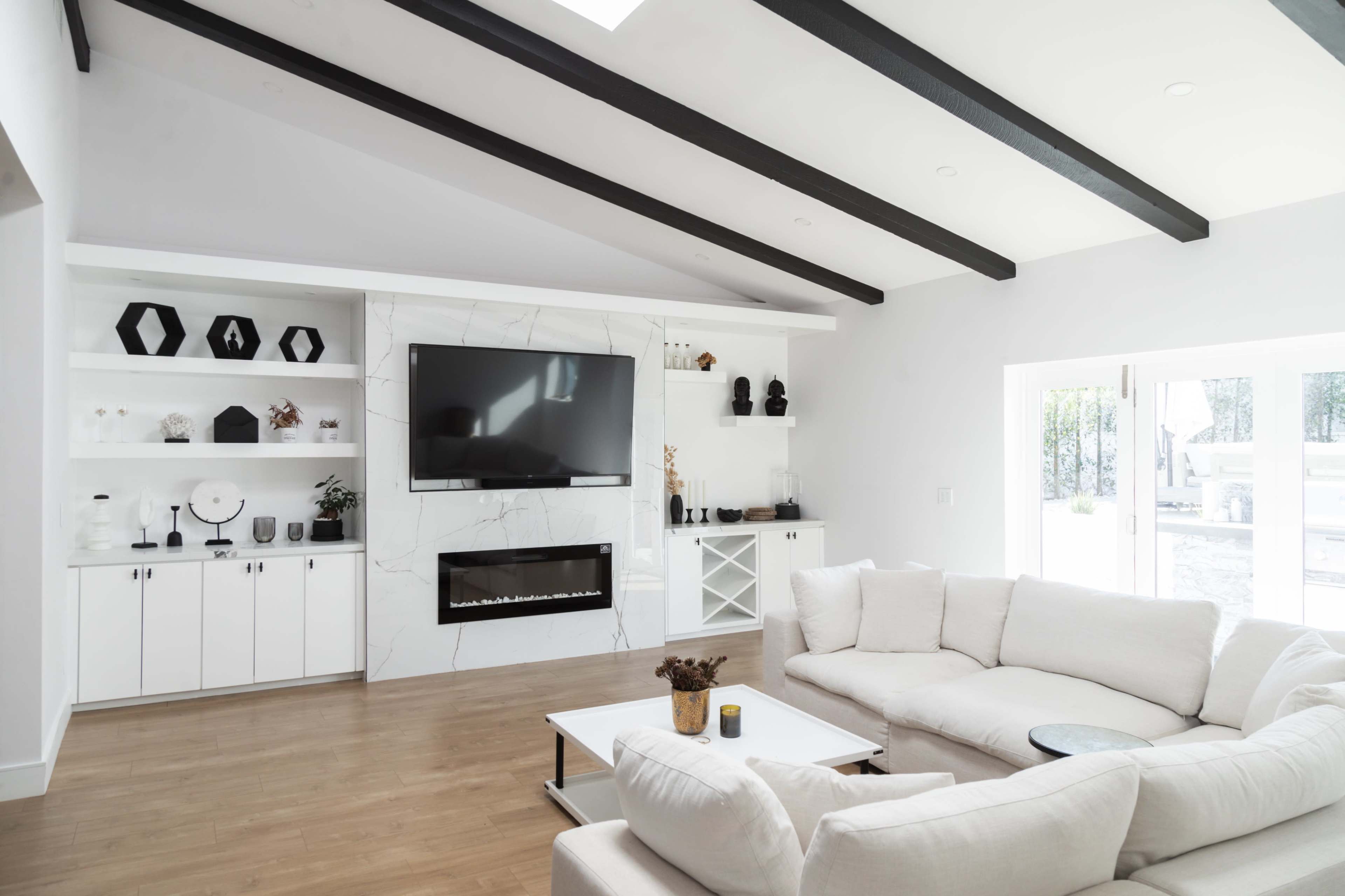 A modern living room featuring a large flat-screen TV mounted on a marble accent wall, flanked by white cabinetry and a light-colored sectional sofa.