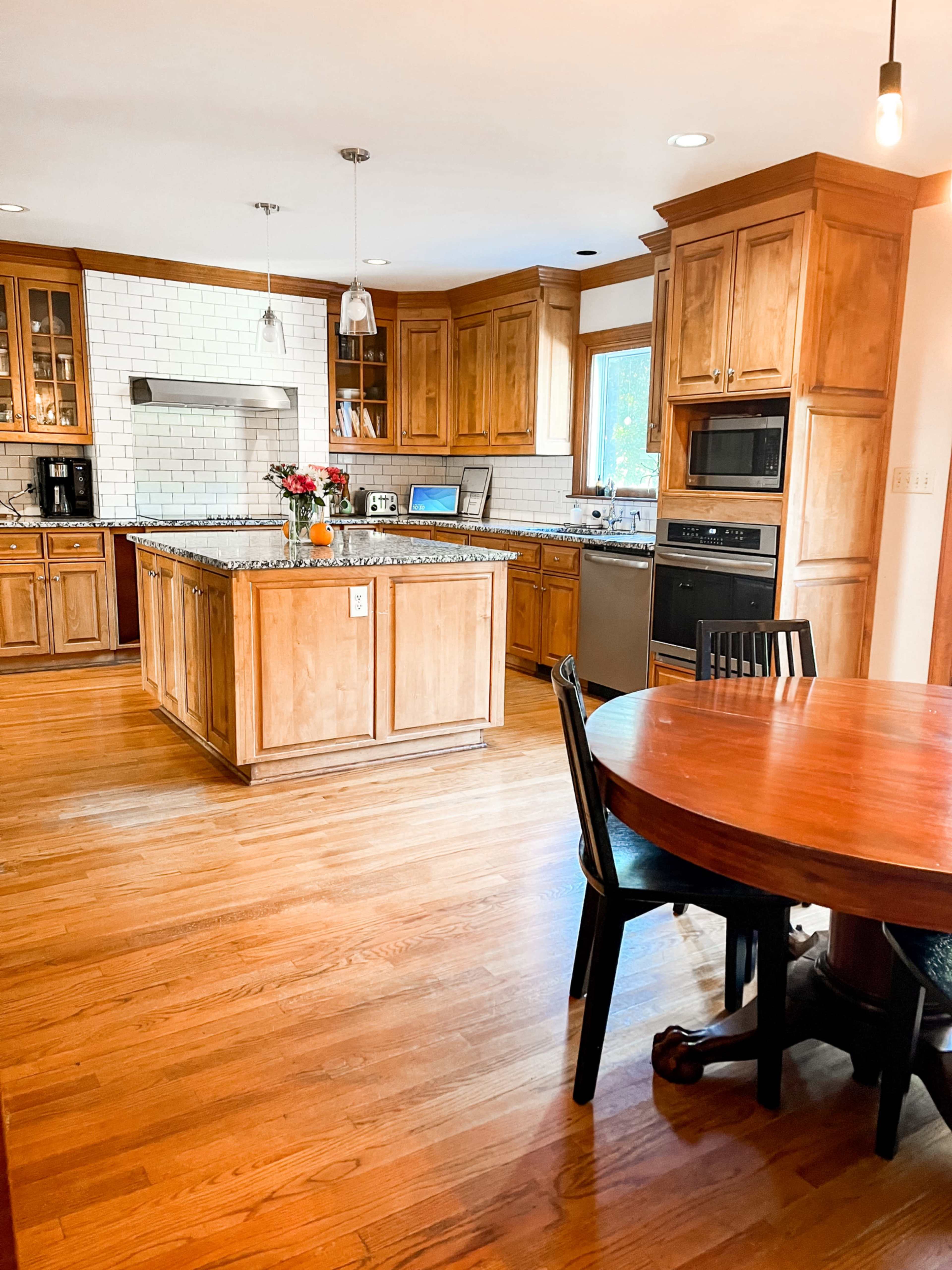 A spacious kitchen features wooden cabinetry, a central island with a granite countertop, and a dining area with a round table.