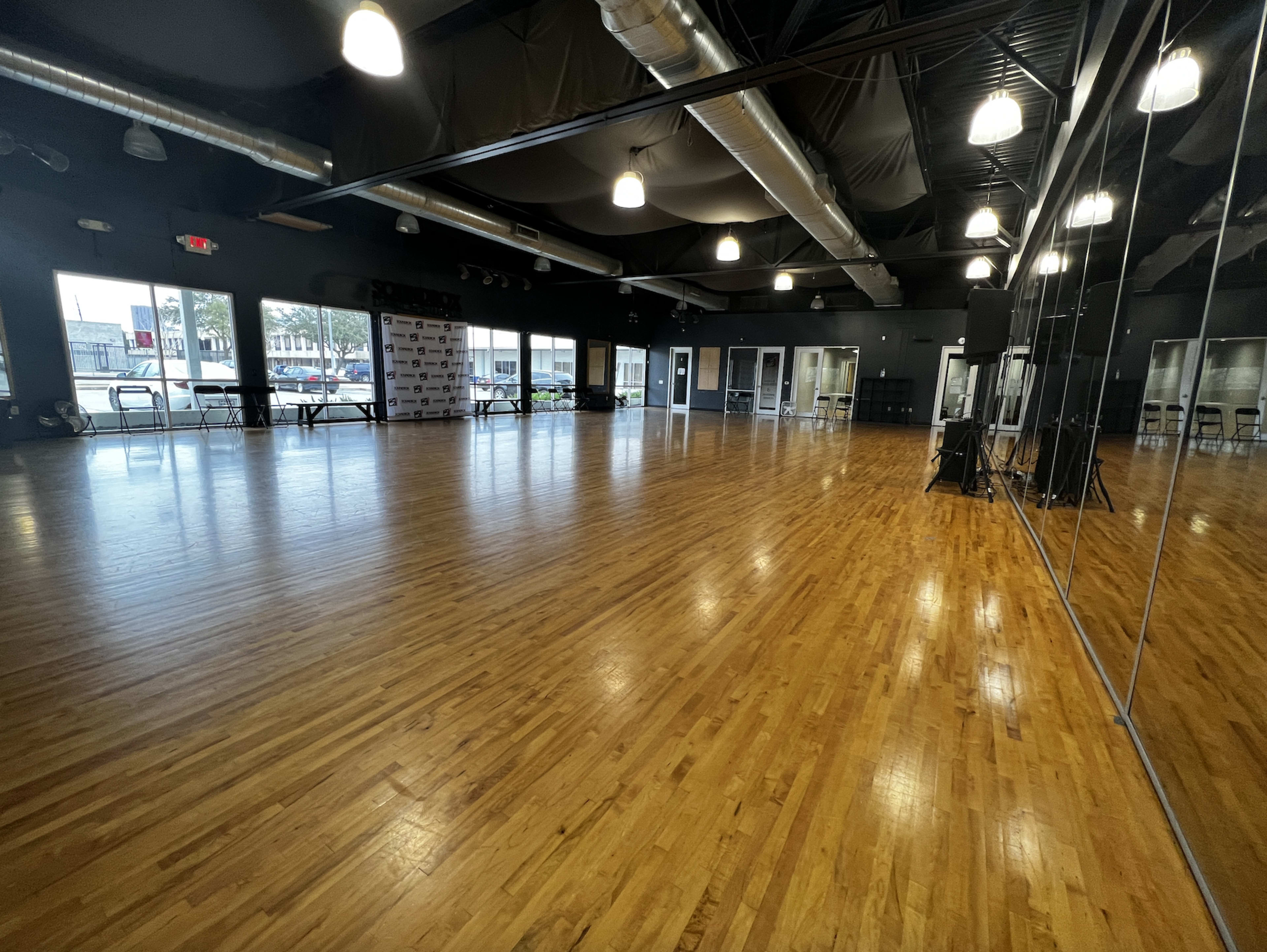 A large, empty wooden-floored studio with mirrored walls and overhead lighting.
