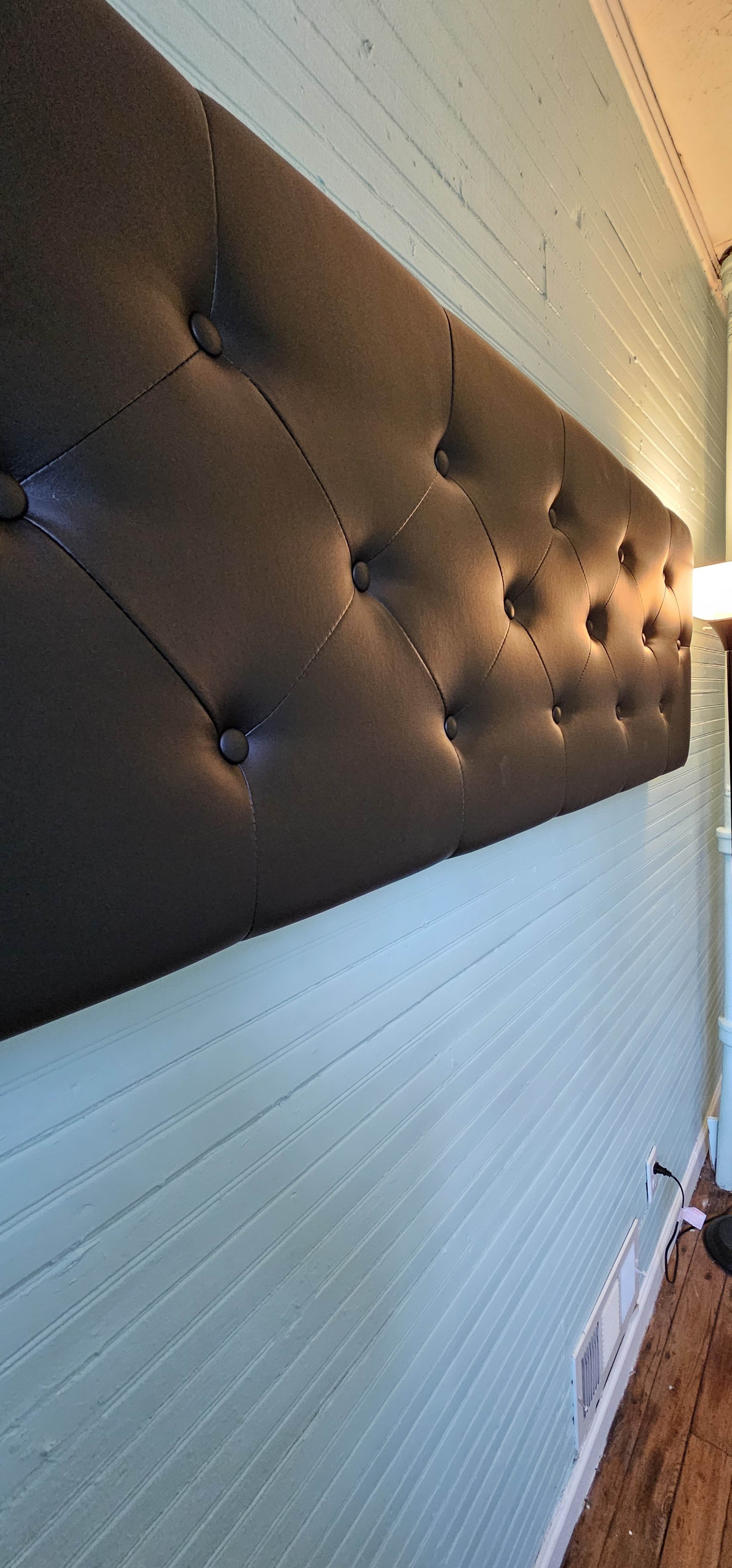 A long, black tufted headboard mounted against a light blue wall with wooden flooring visible below.