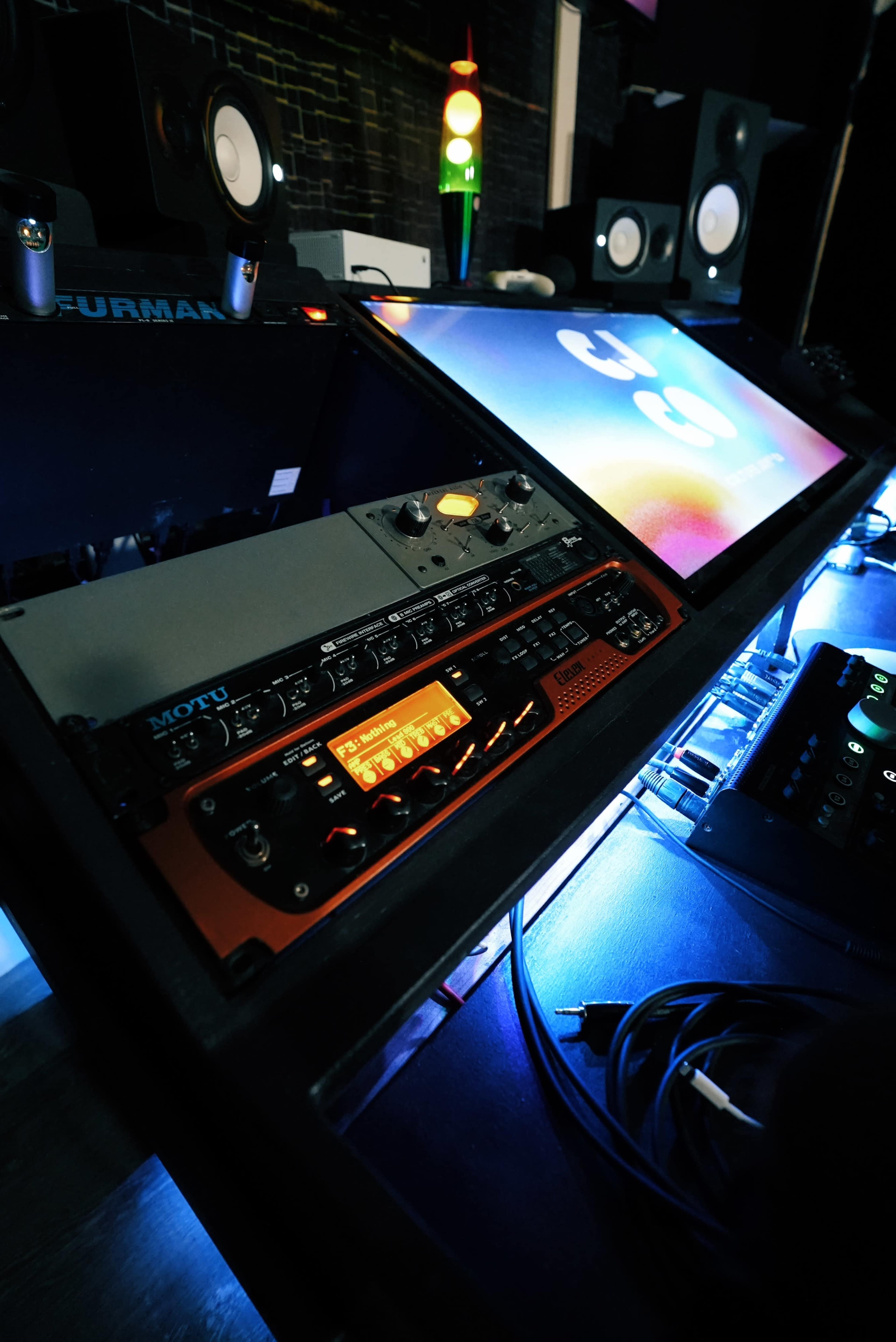 The image shows a close-up of a music production workstation with various audio equipment, including a digital mixer and several monitors.