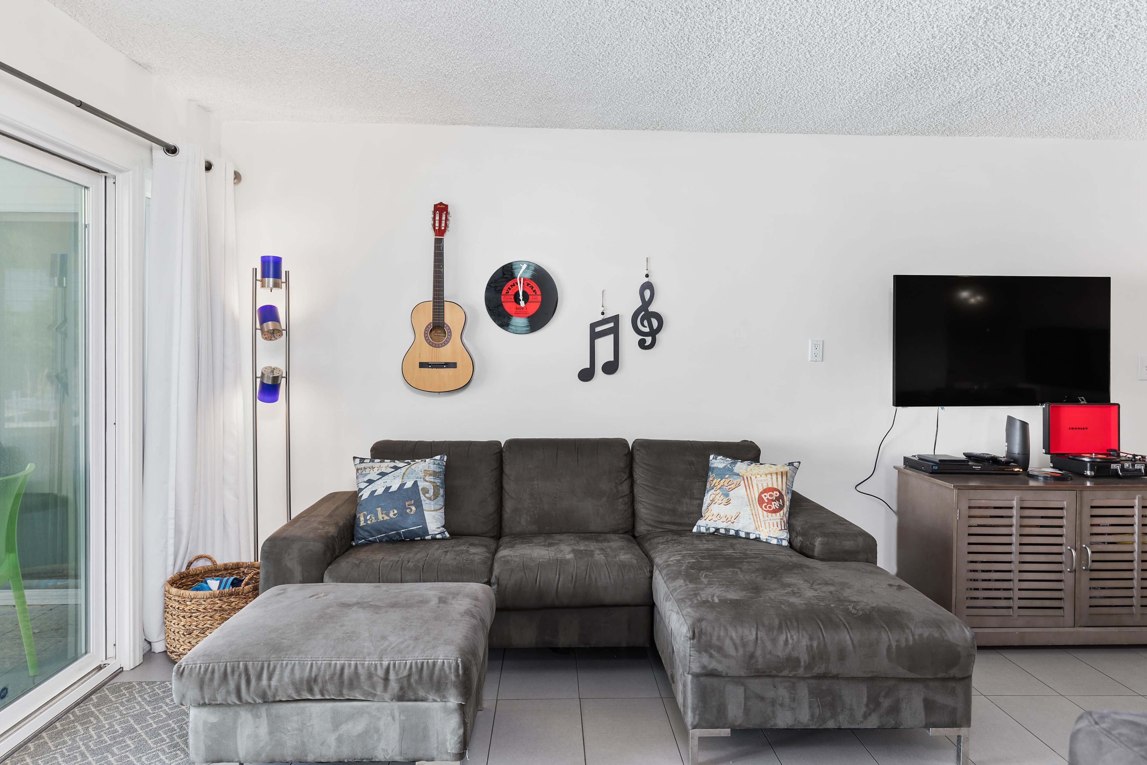 A modern living room features a sectional sofa, a wall with decorative music-themed items, and a television on a wooden stand.